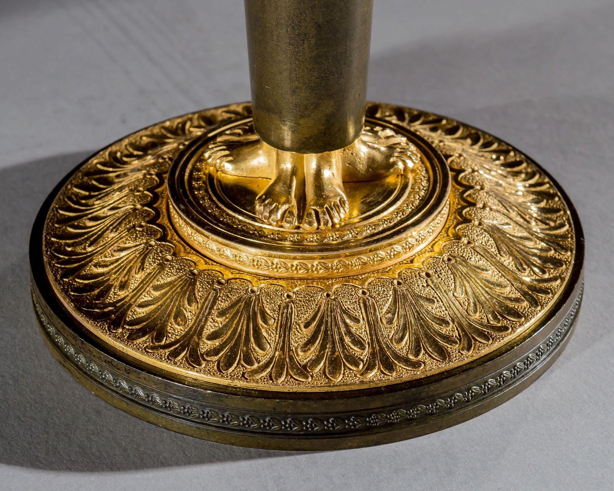 Conjunto de cuatro candeleros de bronce y ormolina, cada uno con una boquilla en forma de urna, fundidos con motivos de hojas tiesas sobre una bandeja de goteo de hojas de acanto. Se apoya en tres cabezas de cariátides femeninas clásicas, sobre un