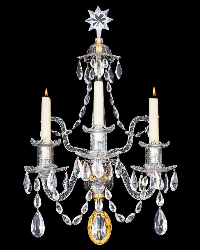 A fine set of ormolu-mounted and cut glass three light wall lights the oval back plates surmounted with a notched cut container supporting the main receiver plate, this supporting two drop hung snake arms and three slip over candle arms these with