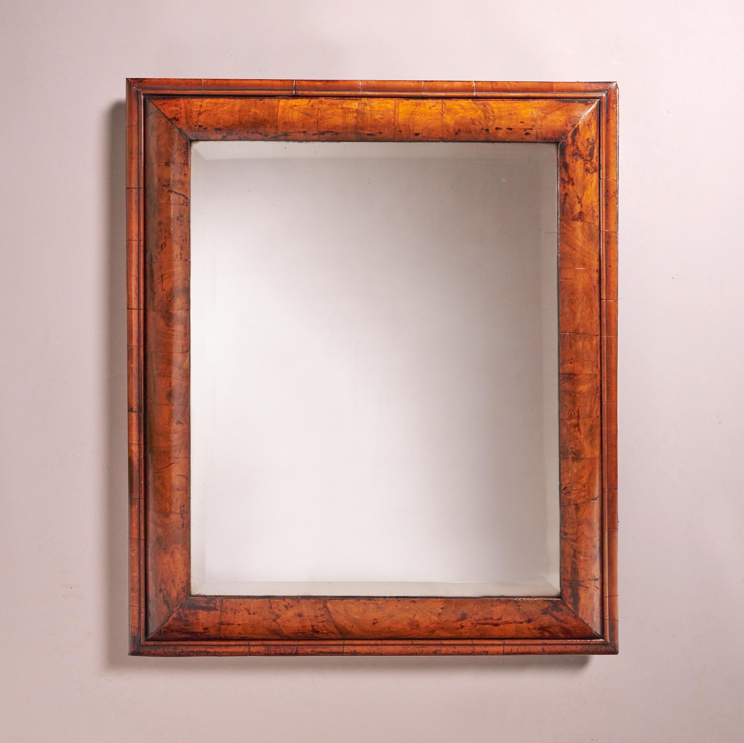 A large William and Mary 17th century figured walnut cushion mirror, circa 1680-1700.

The soft bevelled edge mirror plate is bordered by a pulvinated cushion frame decorated entirely in veneers of well-chosen sections of figured walnut, bordered
