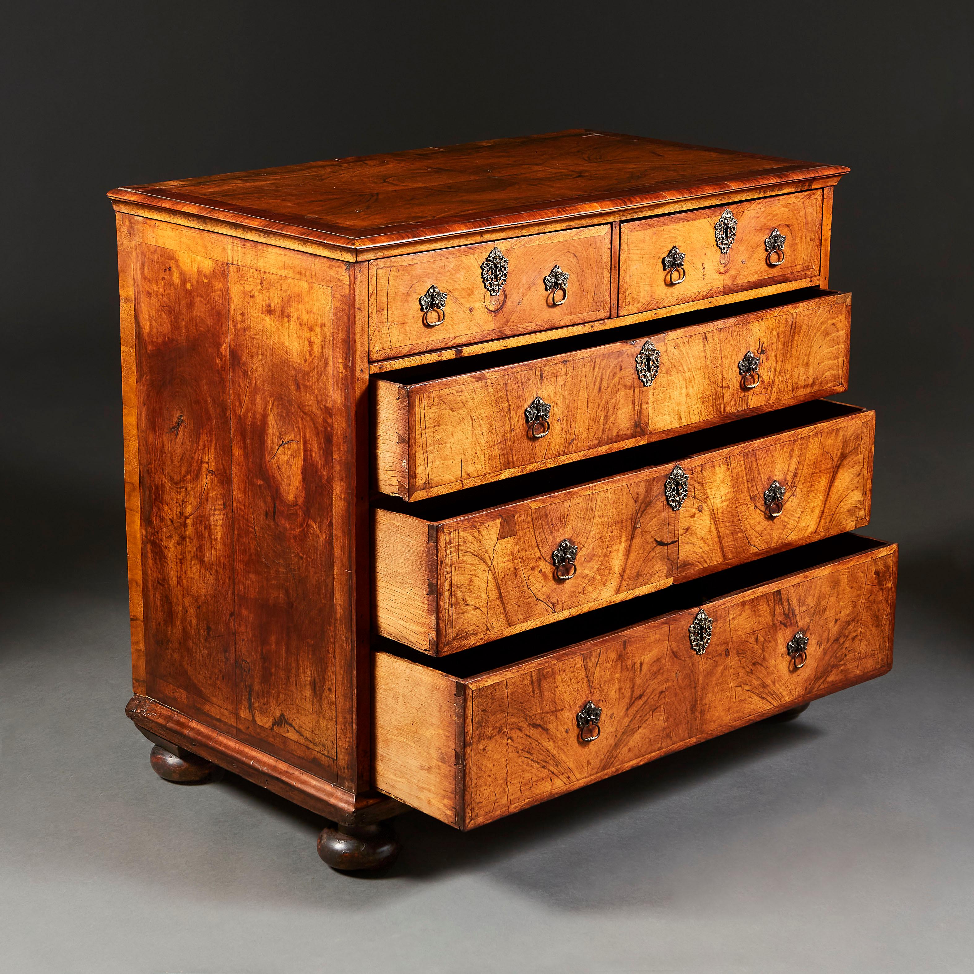 A fine late seventeenth century walnut chest of drawers with three graduated drawers to the front, with two shorter drawers to the frieze, with brass escutcheons and handles with cherub masks, all supported on bun feet. Dated to the underside of the