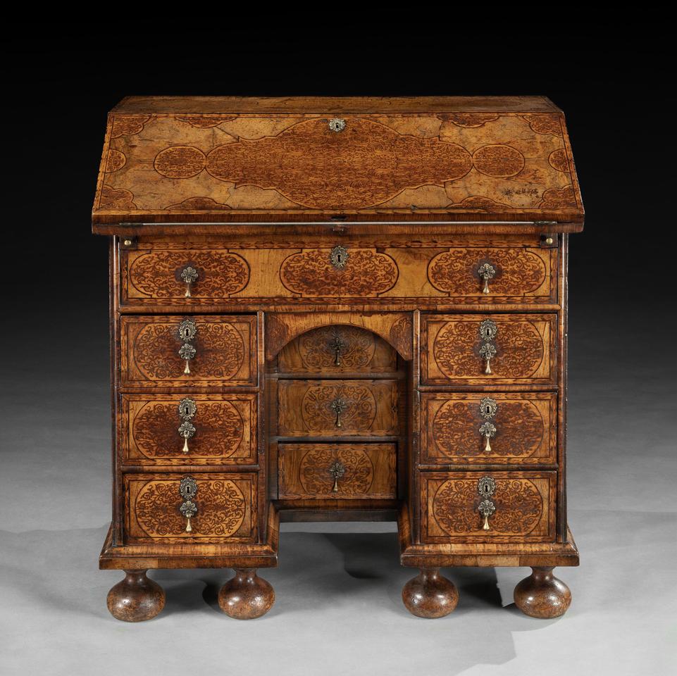 The overhanging upper section with sloping fall profusely inlaid with shaped panels of arabesque seaweed marquetry, framed by burr walnut and foliate borders, enclosing a fitted interior with four short and a long drawer, pigeonholes and a well. The