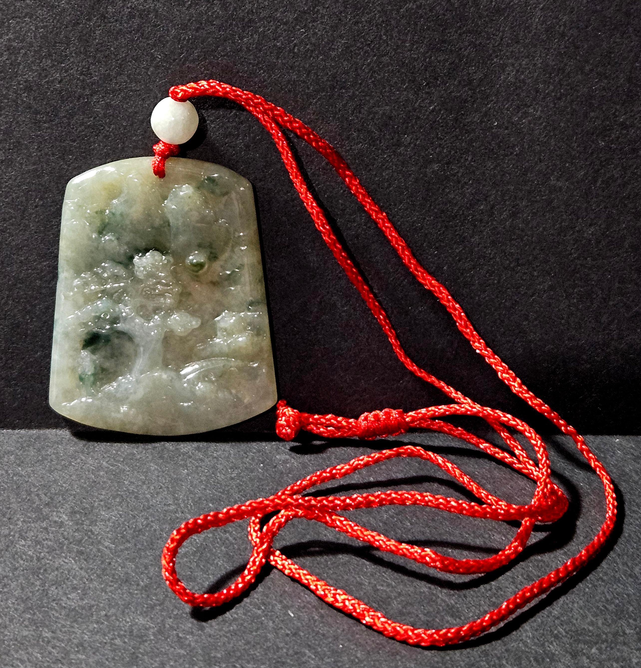 Pendentif en jadéite naturelle du Myanmar Ric#JD001 finement sculpté à la main dans une boîte en bois, représentant un pin et des feuilles sur les rochers avec des couleurs blanches et vertes. Les couleurs semblent être le vert clair et le blanc