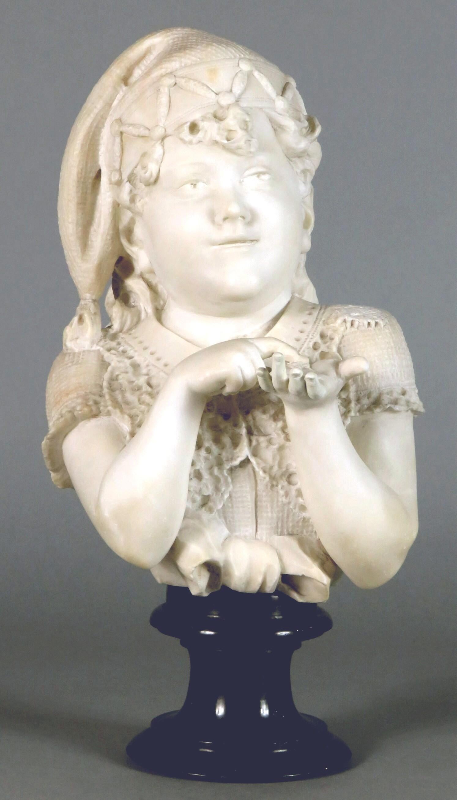 A large & very charming 19th century hand carved Carrara marble portrait bust of a young girl. Shown wearing a tasseled cap while holding the remnants of an object in her left hand, raised overall upon its original verde-antico marble socle. Signed