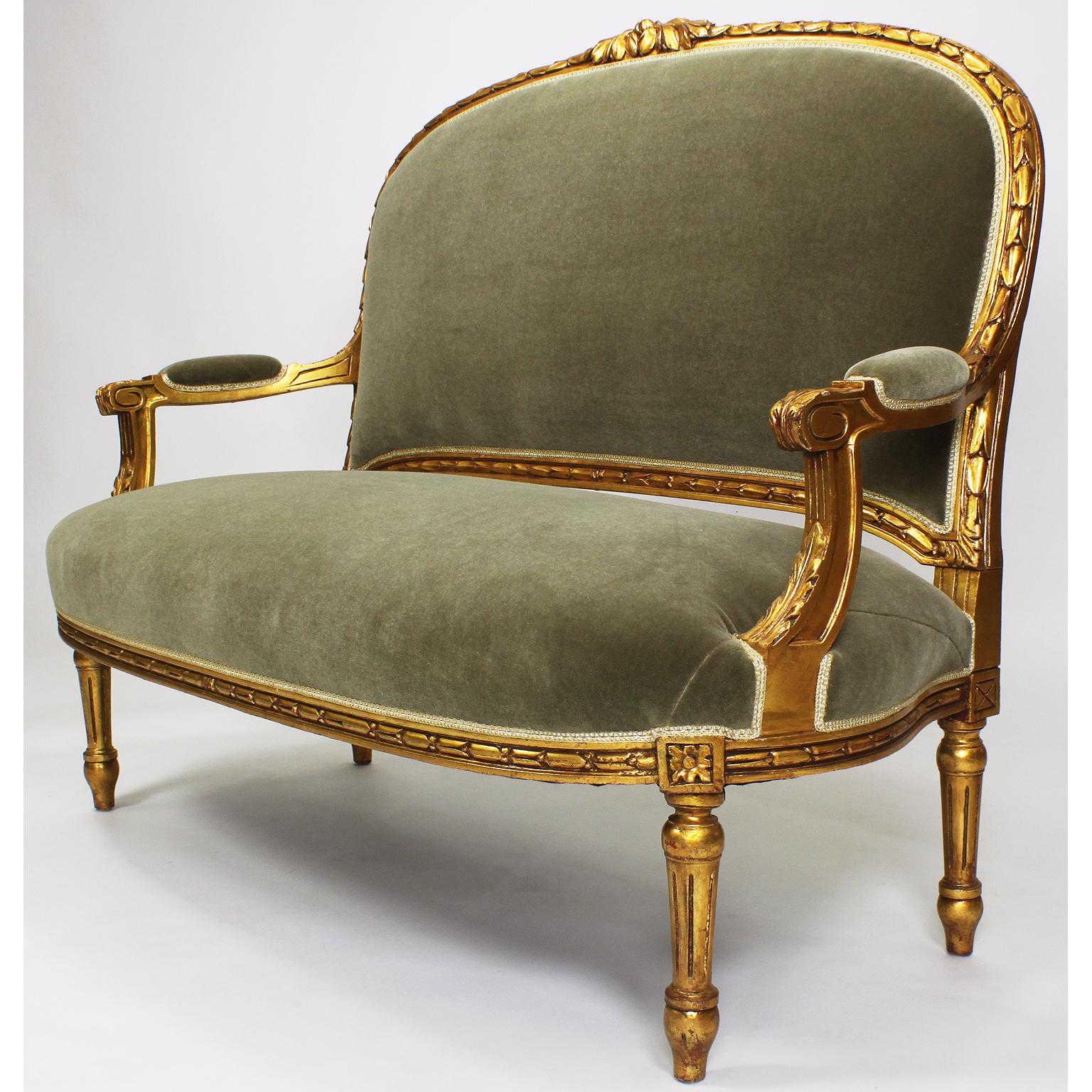 A five piece French Louis XVI style giltwood carved Salon 'Parlor' Suite. The carved gilded wood frame with a floral design and leaves, with padded open armrests and raised on four fluted legs, all upholstered in a recent green velvet, Paris, circa