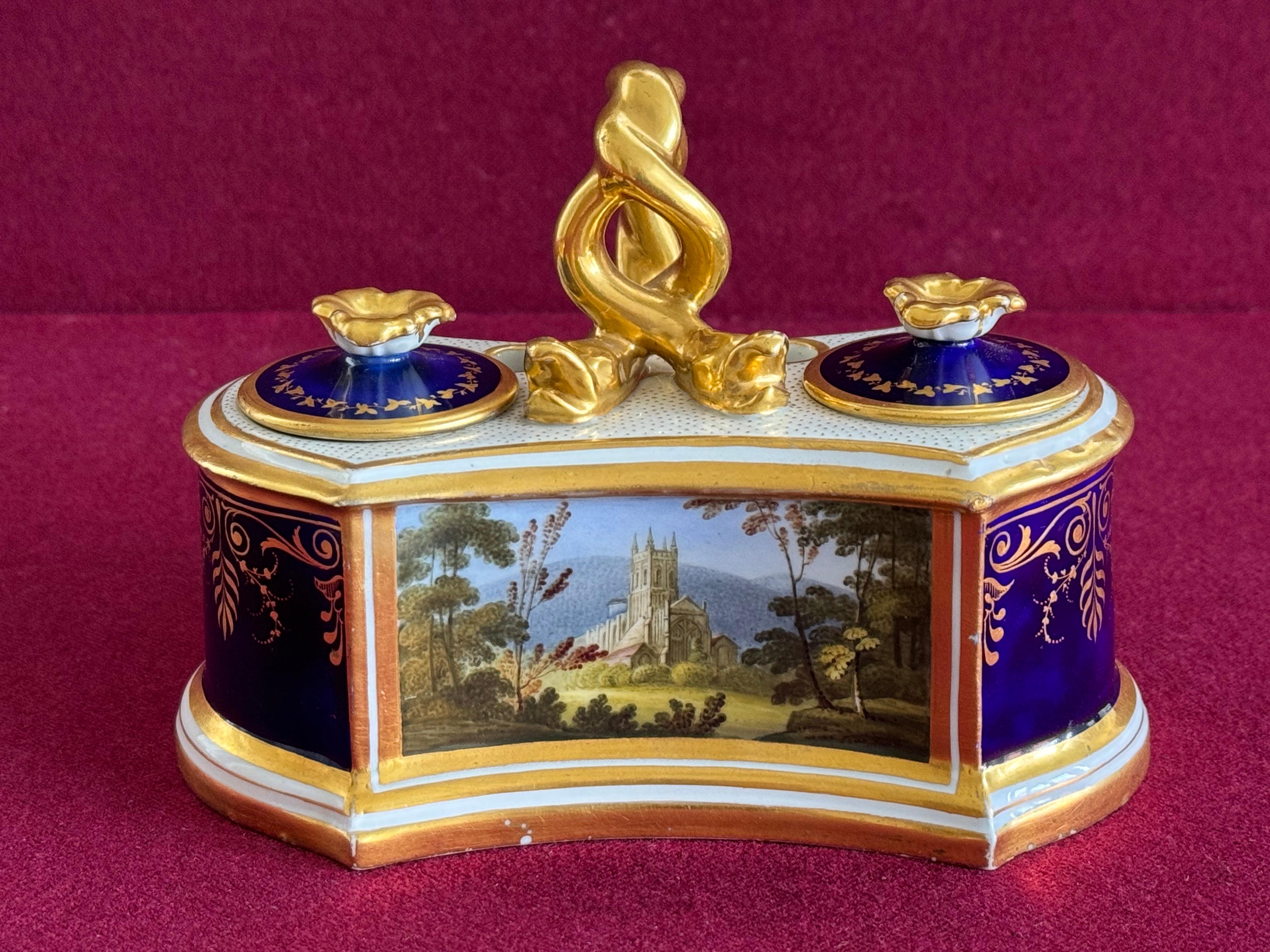 A Flight, Barr and Barr Worcester porcelain inkstand and two covers, c.1815-20. Two fixed inkwells divided by a gilt entwined serpent handle, a pair of quill-holders to the reverse, painted with a large titled panel of 'Malvern Abbey Church