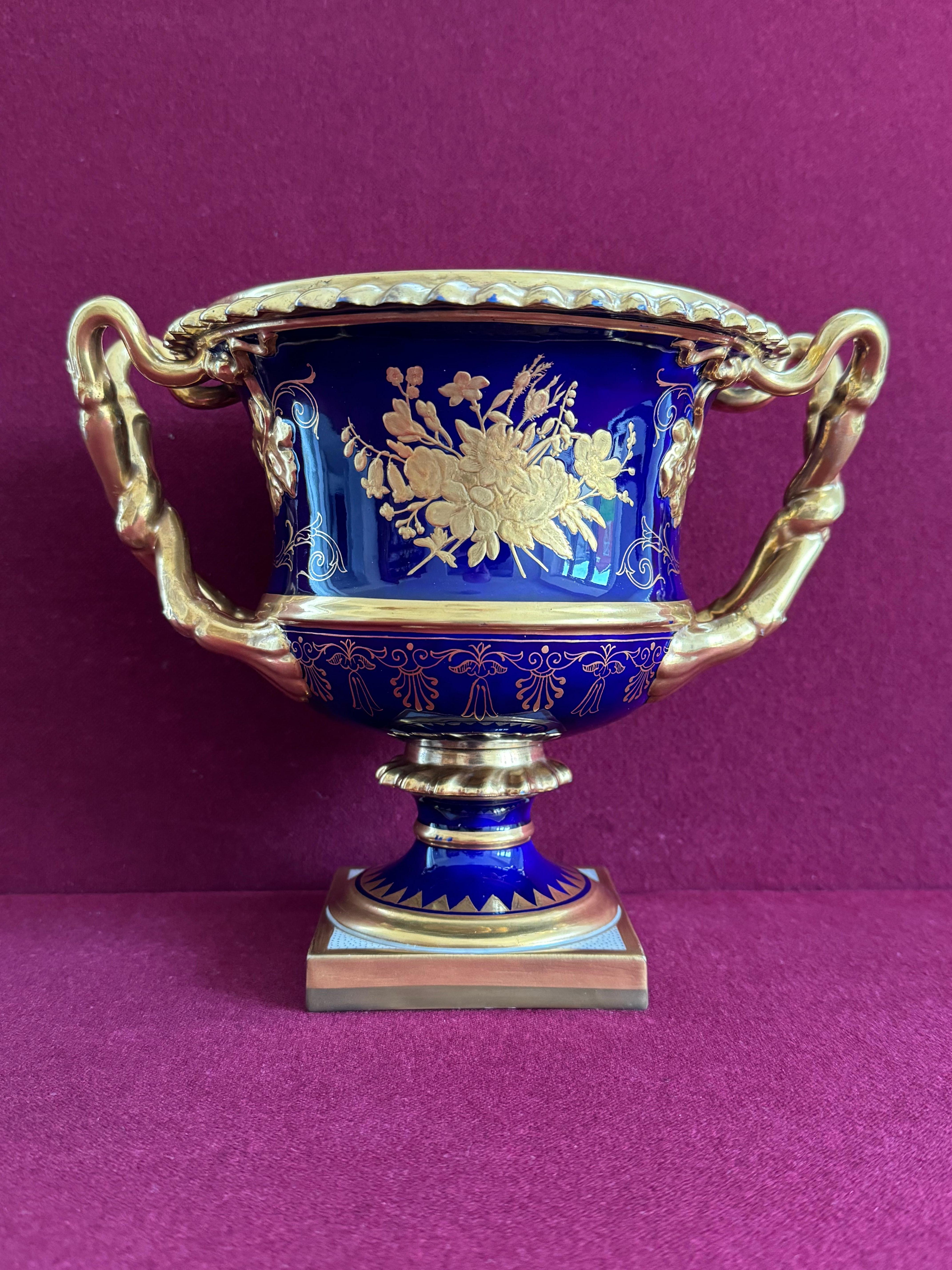 A Flight, Barr And Barr Worcester 'Warwick' Vase, Circa 1815-20. Decorated with a gilt gadrooned rim, gilt twisted double vine stem and leaf handles, and gilded floral and scroll decorative work reserved on a deep cobalt blue ground. Raised on a