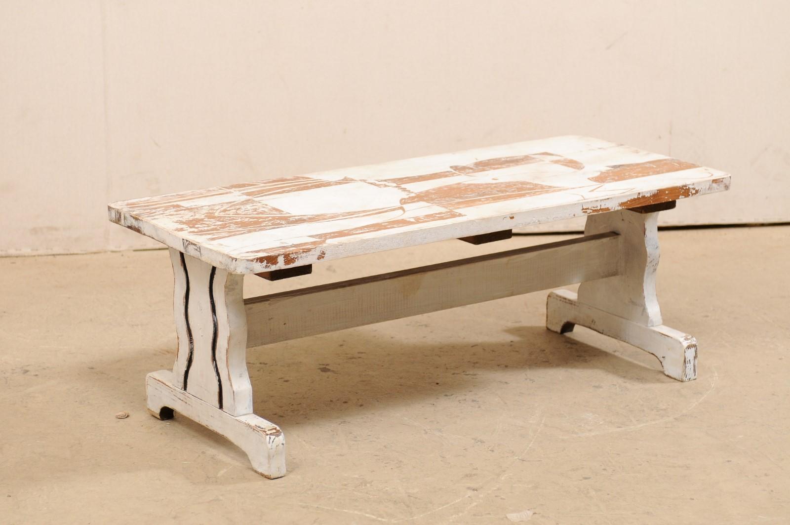 Rustic meets modern in this European Art Deco themed painted coffee table from the mid-20th century. A vintage coffee table from Europe has a rectangular-shaped top, just shy of four feet in length, which is supported by a pair of trestle legs (with