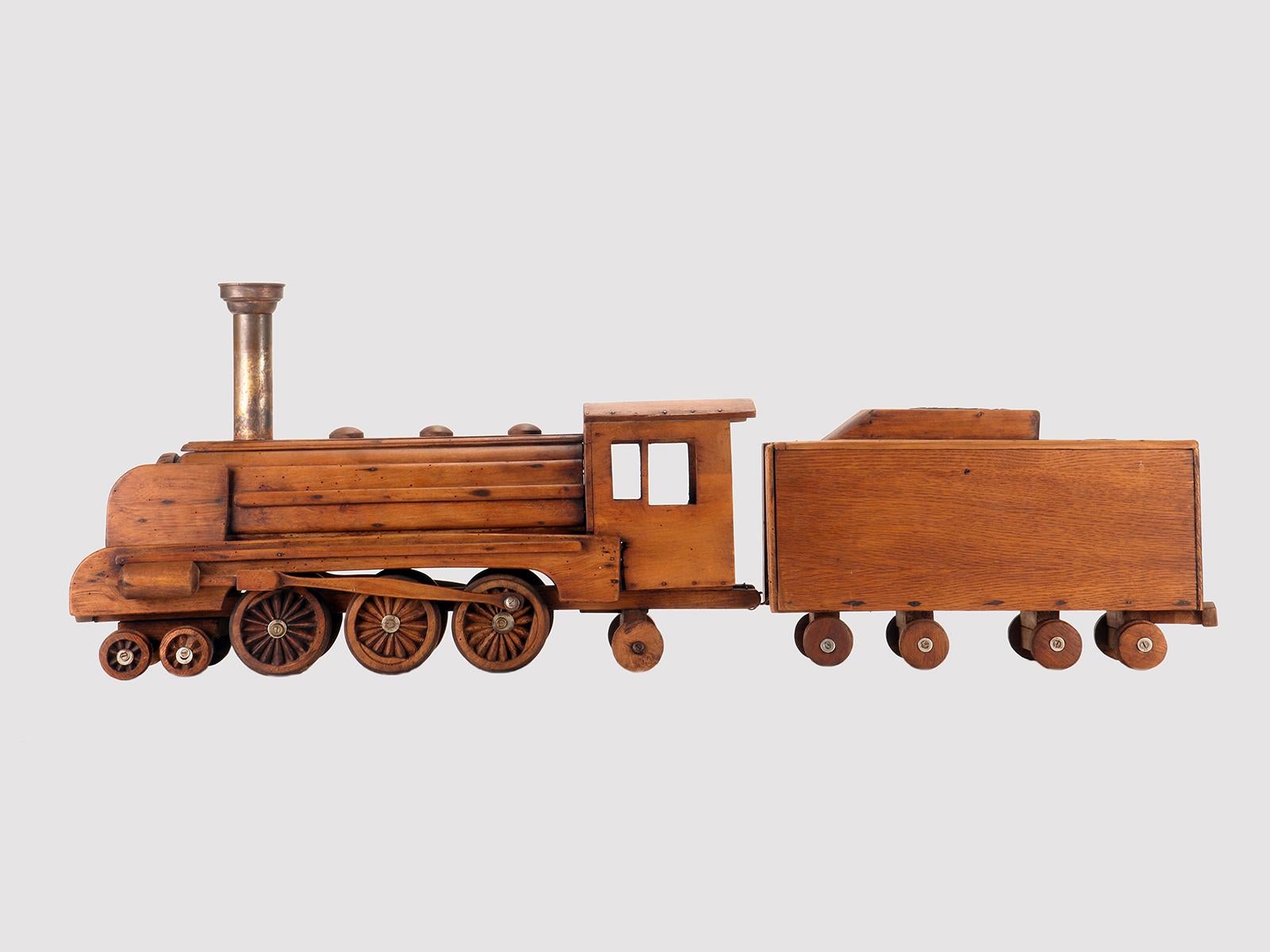 Ein Spielzeugmodell der Volkskunst, Dampfzug, bestehend aus zwei Elementen, der Lokomotive und einem Kohlewagen. Aus Eichenholz mit Metalldetails. Der Schornstein ist, wie die runden Elemente, die im oberen Teil verlaufen, aus Messing mit Spuren von