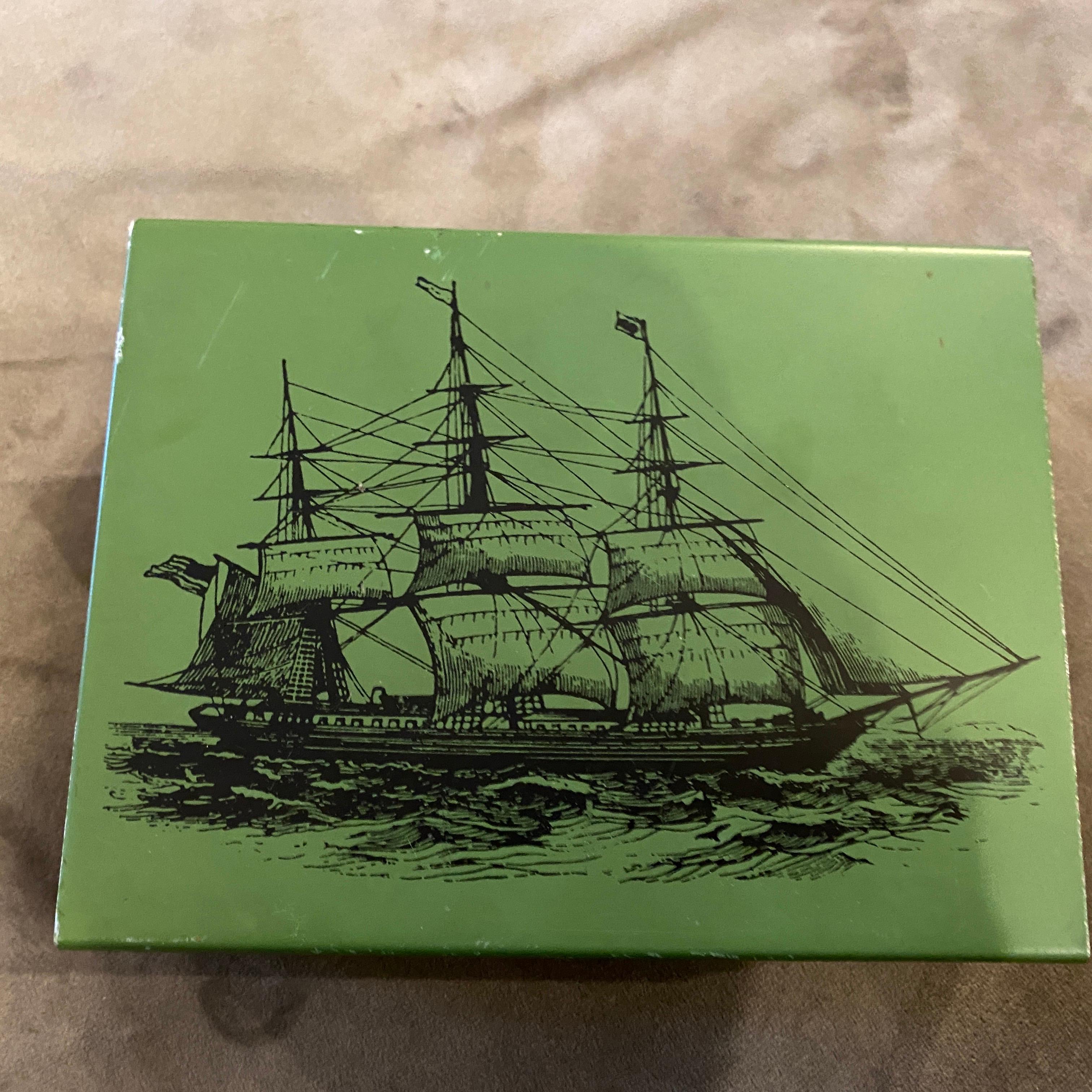 A decorative box designed by Piero Fornasetti and manufactured by Atelier Fornasetti, It has a green metal cover with a black sailing ship, typical of Piero Fornasetti and a mahogany inner compartment. The bottom part is grey felt. 
