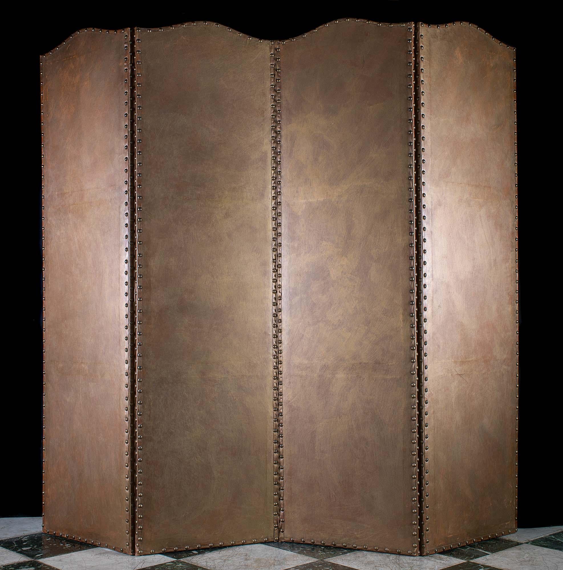 An ornate four fold leather backed canvas screen with applied paper panels held by leather bands and metal stud work. Each panel is painted in the Baroque manner with depictions of birds, vines and flowers within decorative borders. The panels are