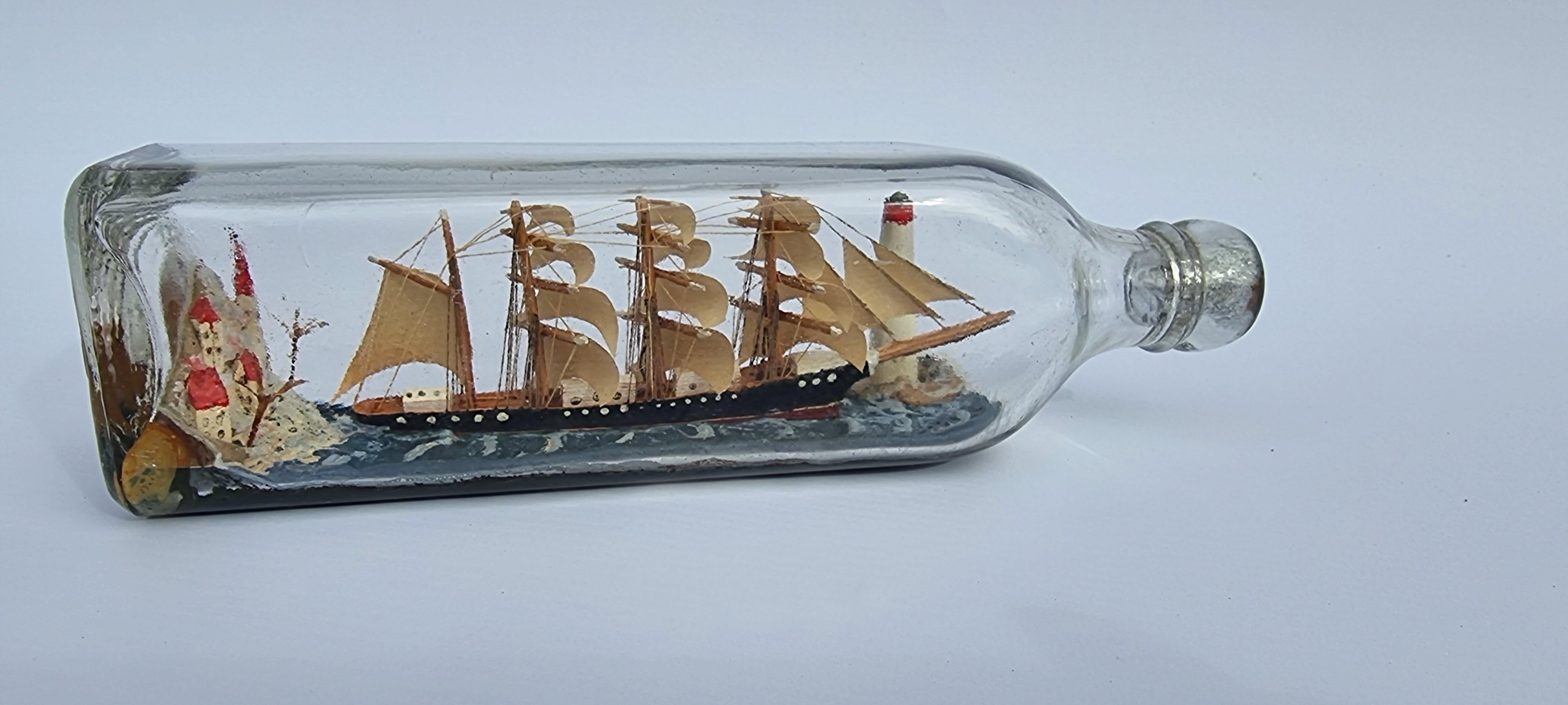 
This very good example has been hand built in a smaller sized square bottle than normally seen. It contains a large four mast 18th century ship fully rigged and with open sails leaving the shoreline which has high cliffs and buildings whilst about