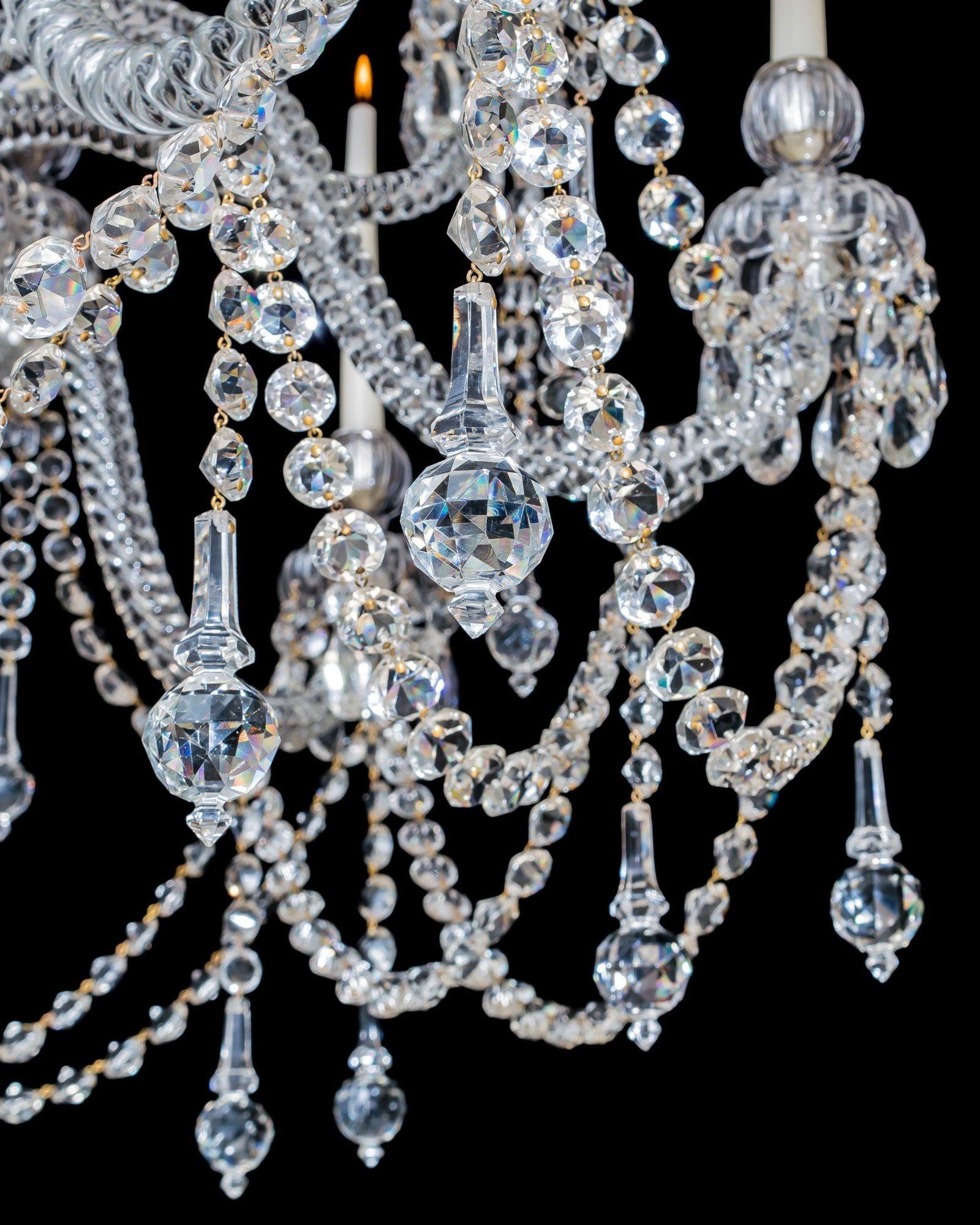 The scroll crook corona above a multi baluster stem, issuing fourteen rope twist arms supporting drop hung drip pans and candle nozzles. The chandelier profusely draped with half back spangles and Osler's signature lapidary cut ball finals.
