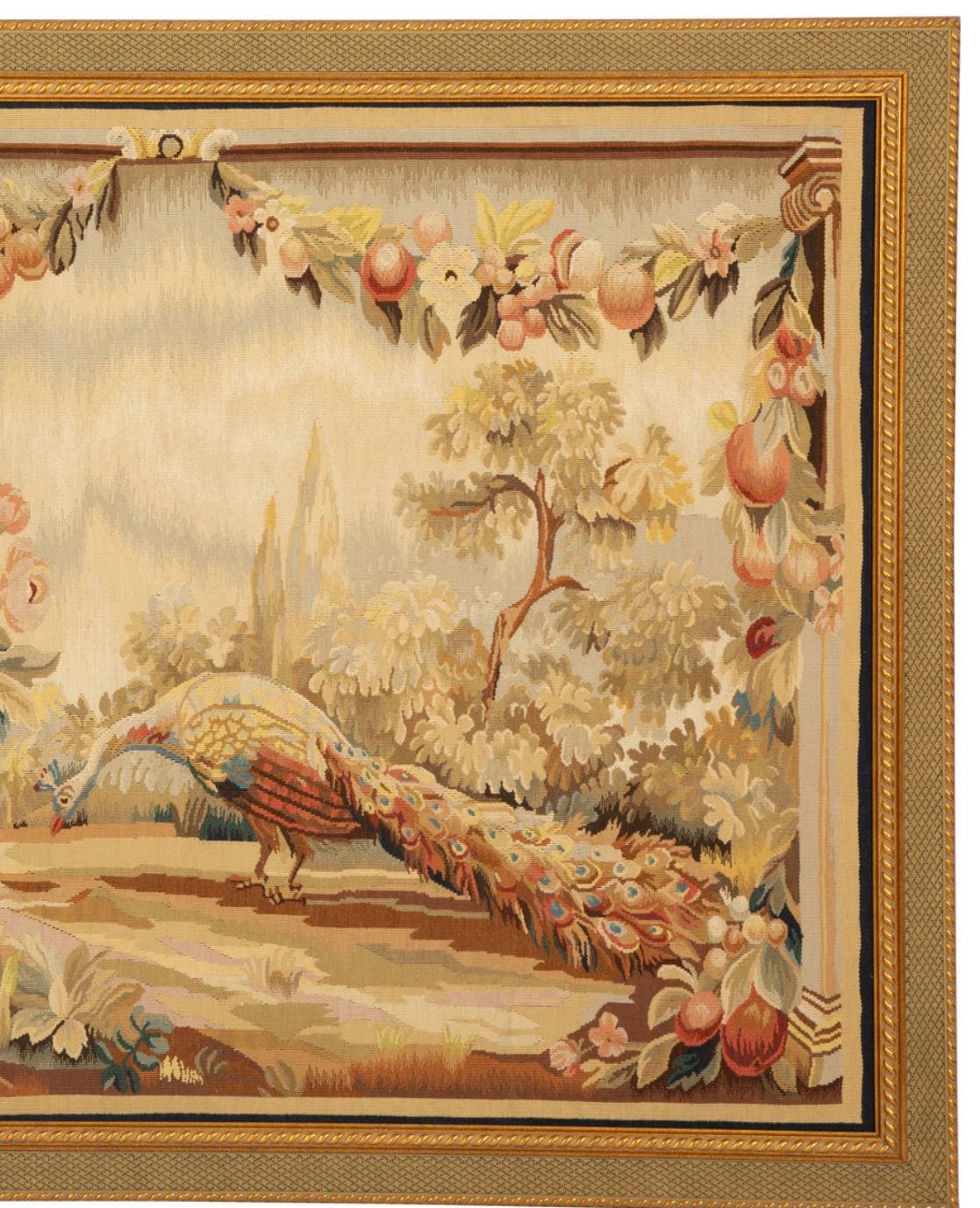 French Aubusson tapestry with a peacock in a wooded landscape next to an urn of flowers. Swags of flowers along the top in shades of pale red, greens and browns. and framed in a gold giltwood frame. Framed and ready to hang.