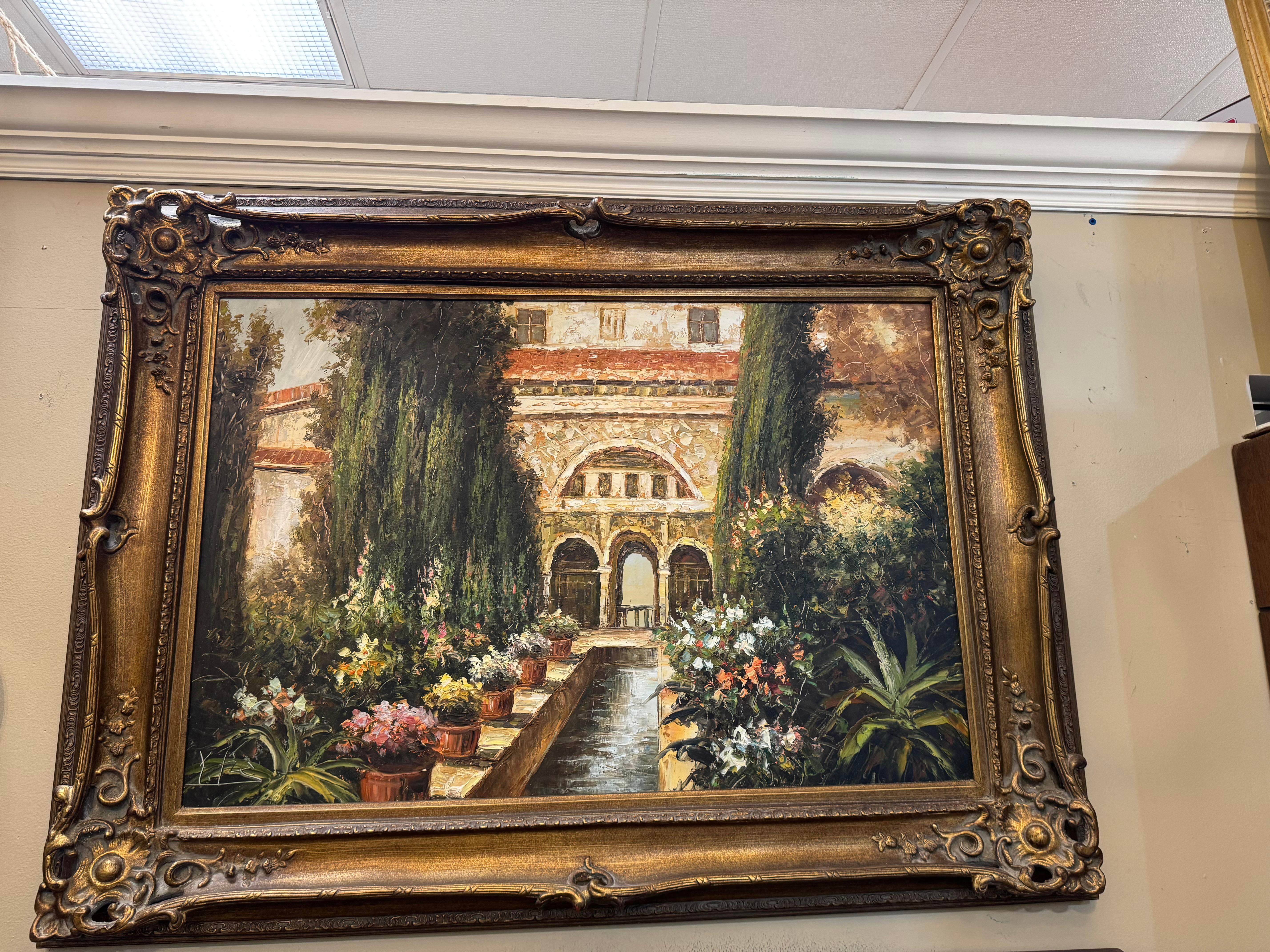 un tableau encadré représentant une cour ou un jardin, peut-être dans un style européen ou méditerranéen.
Sujet :
Le tableau représente un bâtiment avec des arcades, entouré d'une végétation luxuriante et de plantes en pot. Le centre est traversé