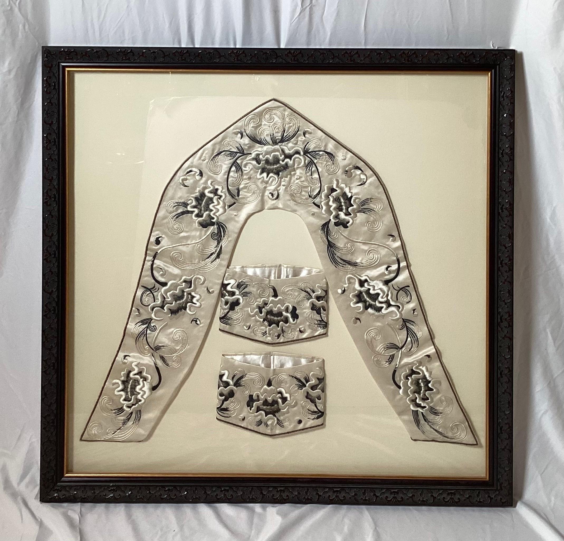 A beautifully framed set of hand embroidered silk vestments. The sash-collar and cuffs in a floral black and off white palette on a white silk background. The frame with a beautiful carved Hung Mu wood frame.