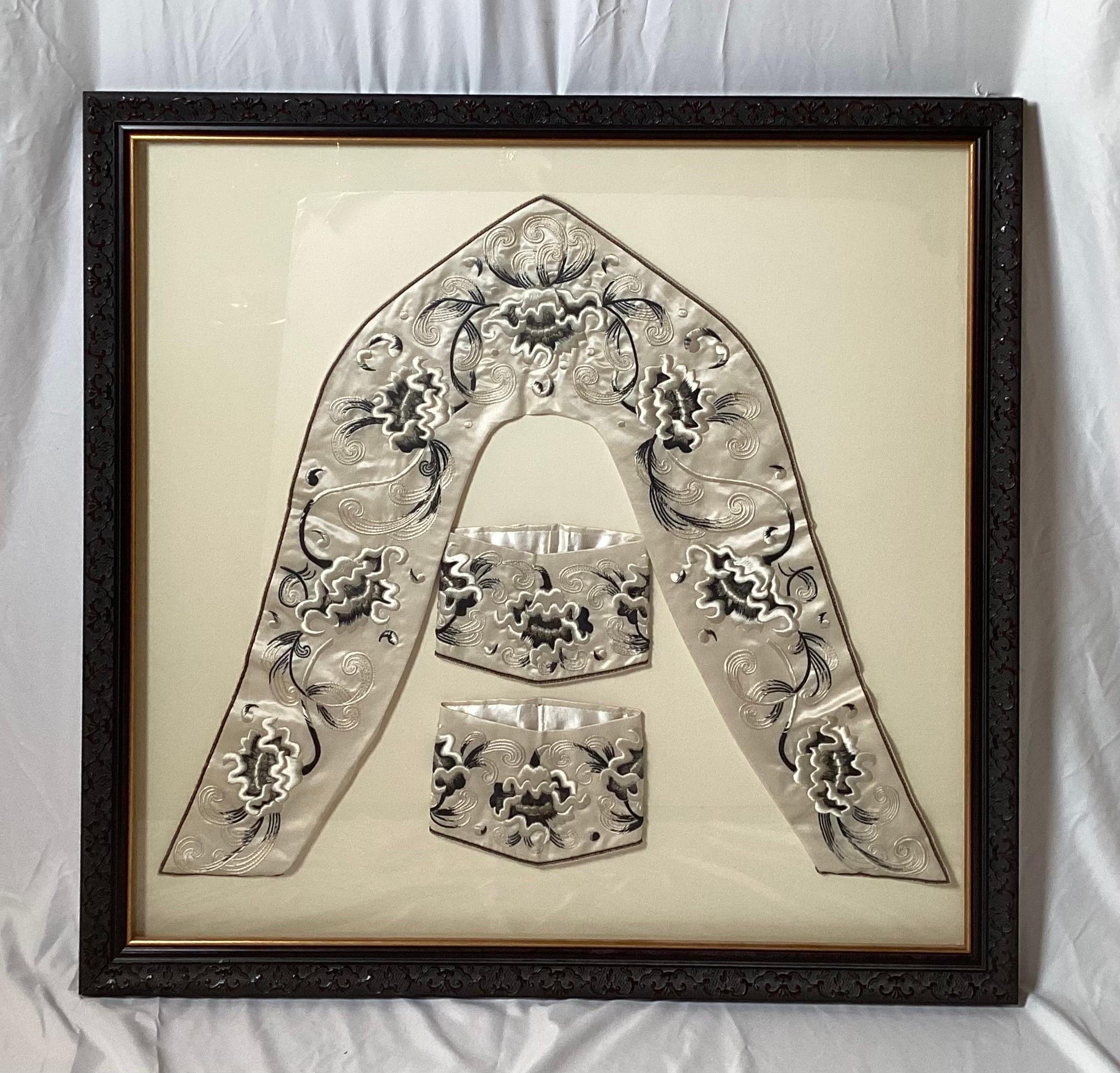 Un ensemble magnifiquement encadré de vêtements en soie brodés à la main. Le col et les poignets de la ceinture dans une palette florale noire et blanc cassé sur un fond de soie blanche. Le cadre est constitué d'un magnifique cadre en bois sculpté