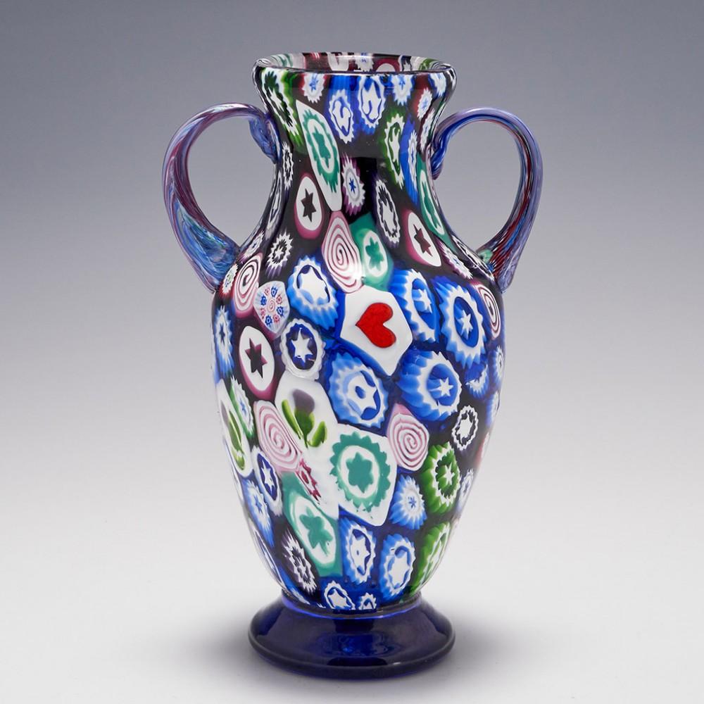Heading : A Franco Toffolo John Deacons silhouette paperweight vase
Date : 1990's
Origin : Scotland
Features : Two handled vase cased with silhouette millefiori canes on a clear ground with a clear glass blue foot
Marks : Signed Franco Toffolo,