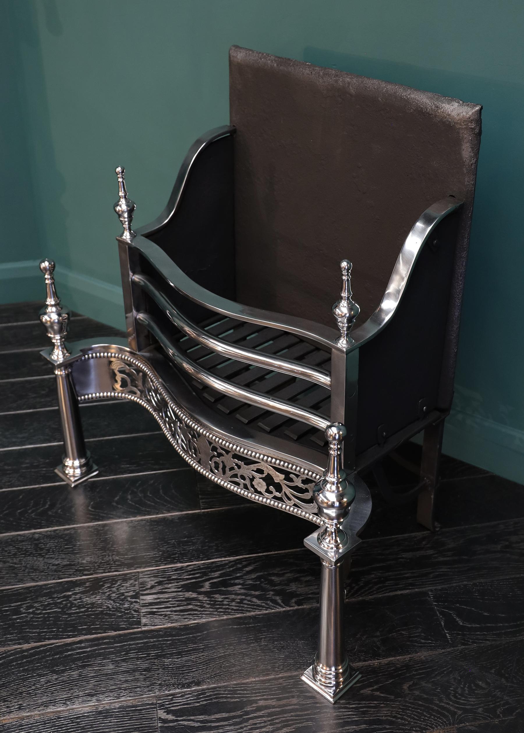 Grille de foyer autoportante en acier poli de forme géorgienne. La corbeille à feu avec trois barres à feu au-dessus d'une frette ajourée et ornée, soutenue par des pieds cyclindriques avec des fleurons en forme d'urne stylisée. Cette offre concerne