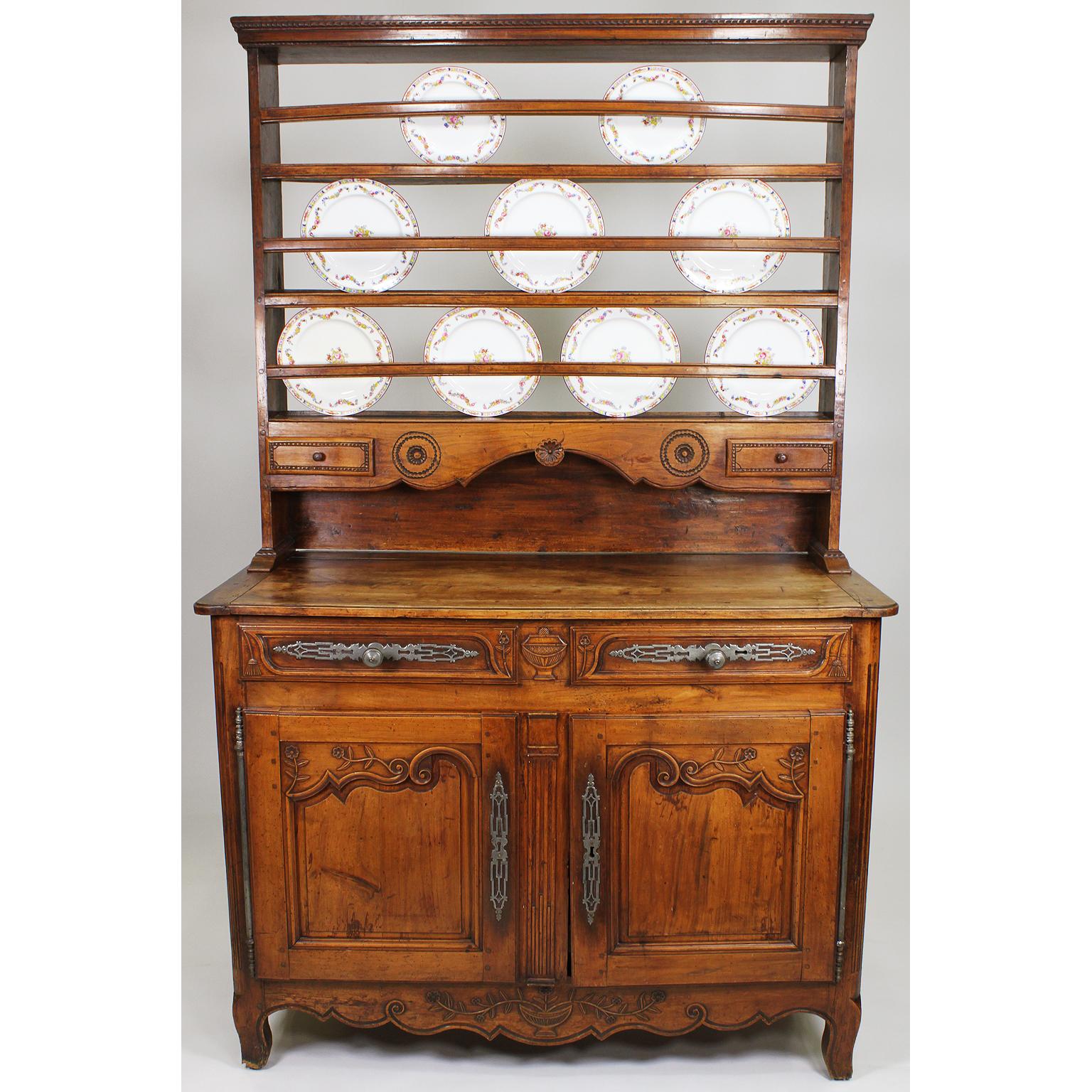 A French 18th-19th century Provincial Louis XV style carved walnut Vaisselier hutch buffet. The rectangular body with twin apron drawers with hammered silvered-metal hardware, centered with a carved urn above a pair of cupboard doors with fiche