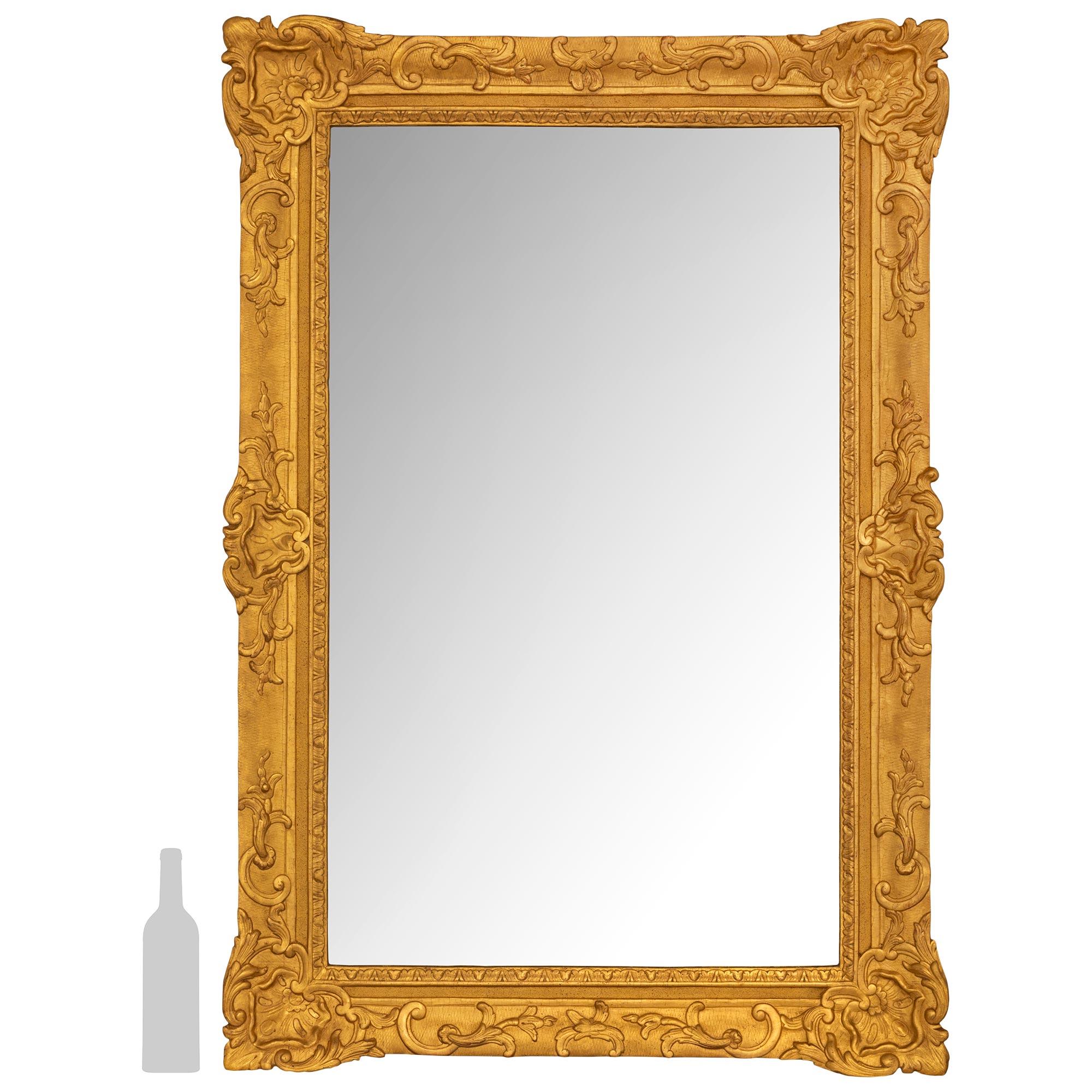 An elegant French 18th century Regence period rectangular giltwood mirror. The mirror showcases a stunning frame with a lattice designed background with foliate reserves on the corners with a central shell like design. The reserves are flanked by