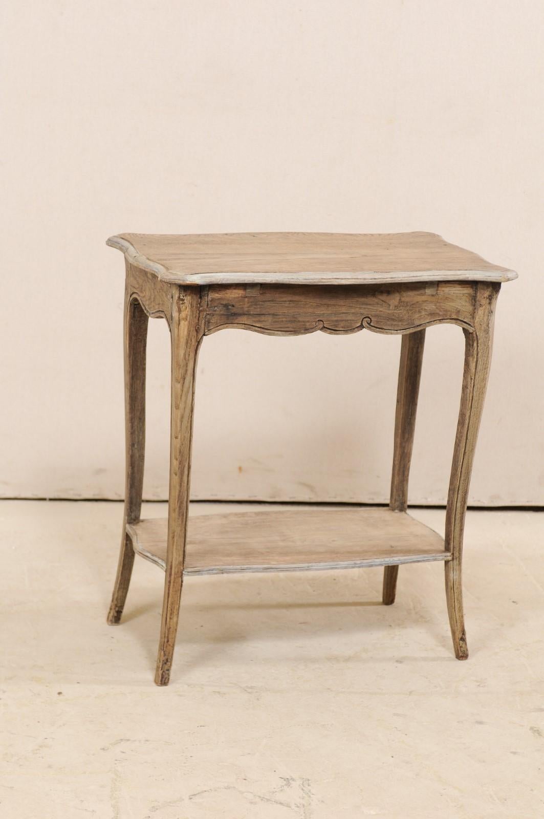 A French two-tiered end table from the 18th century. This antique table from France was created with delicate features; the rectangular-shaped top is edged with scalloped carving, which is then repeated about all sides of the apron beneath. The top
