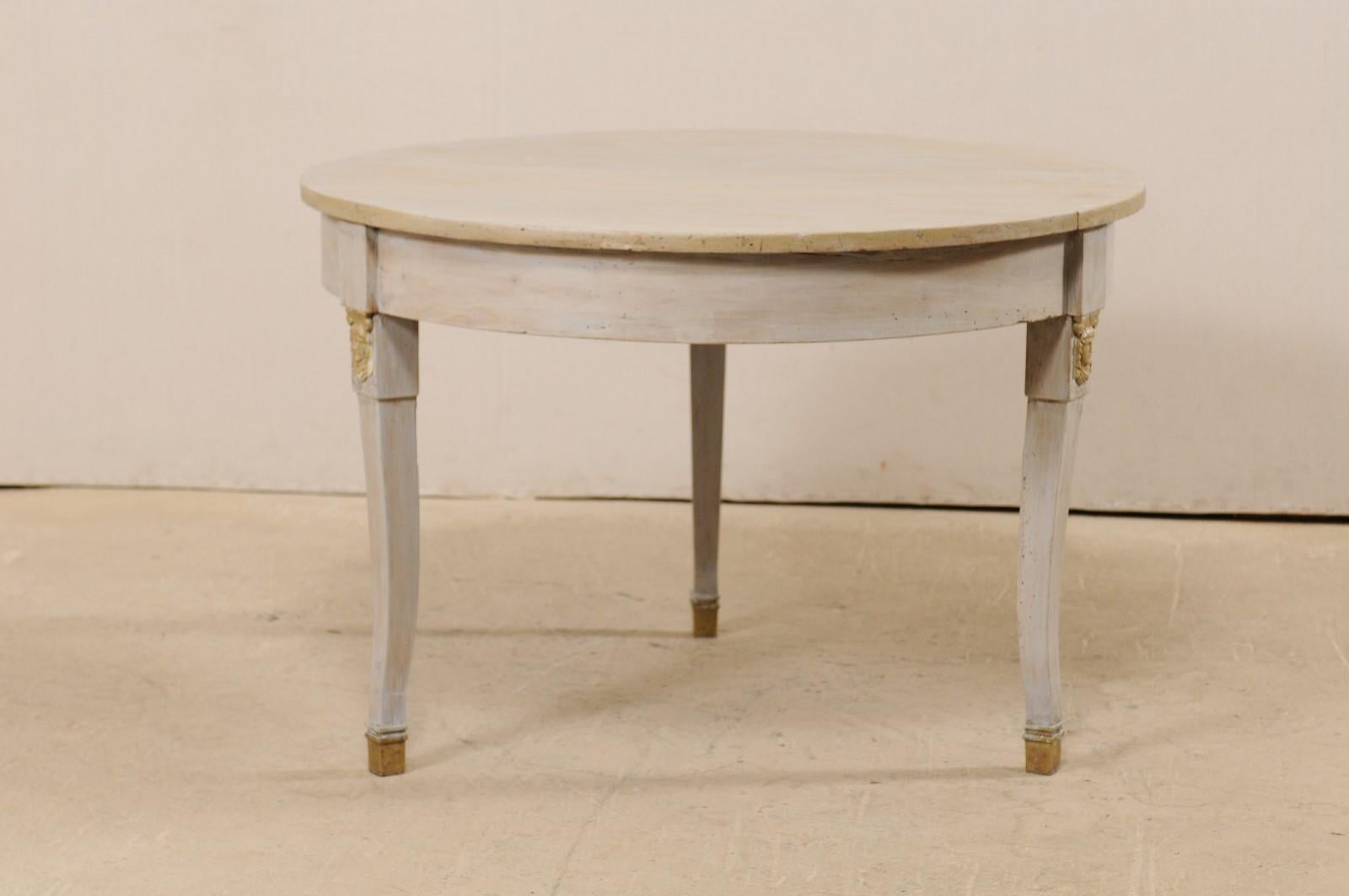 A French painted wood center table from the 1920s. This antique table from France features a circular-shaped top with nicely carved and rounded apron, which is raised on gently curved legs with facial carvings at the knees, and terminate into