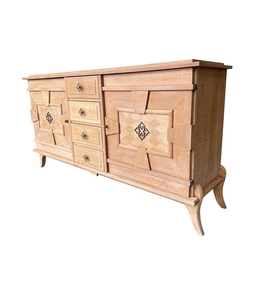 A French 1940s bleached solid oak sideboard with four drawers and two doors both with wonderful marquetry detail and original brass handles and flower design. With harlequin marquetry top and curved and shaped feet.   