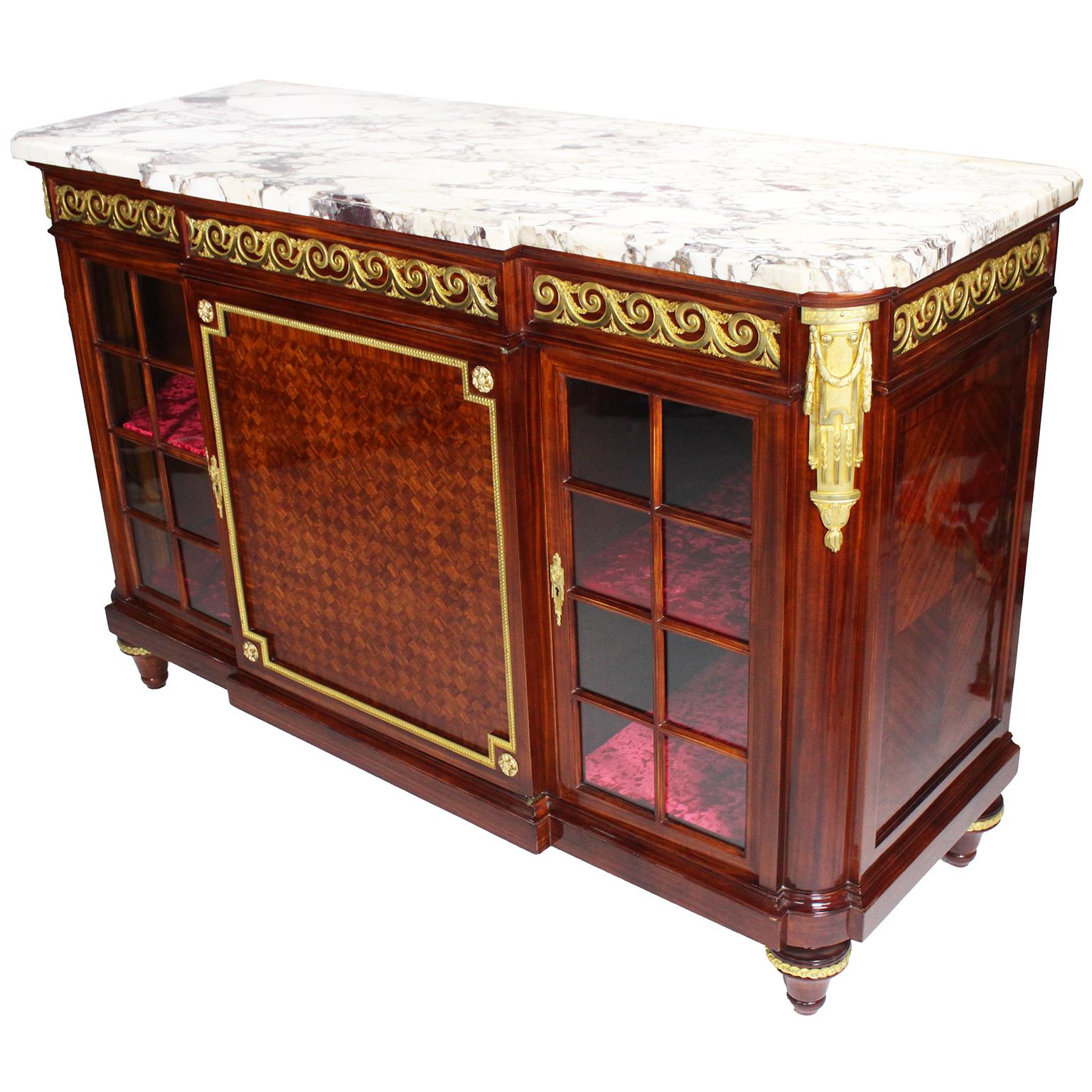 Un raffinato e raro commode-server francese del XIX-XX secolo in stile Luigi XVI con montatura in mogano e intarsio satinato, attribuito alla Maison Forest. Il corpo rettangolare è sormontato da un piano in marmo brèche violette sopra un fregio con