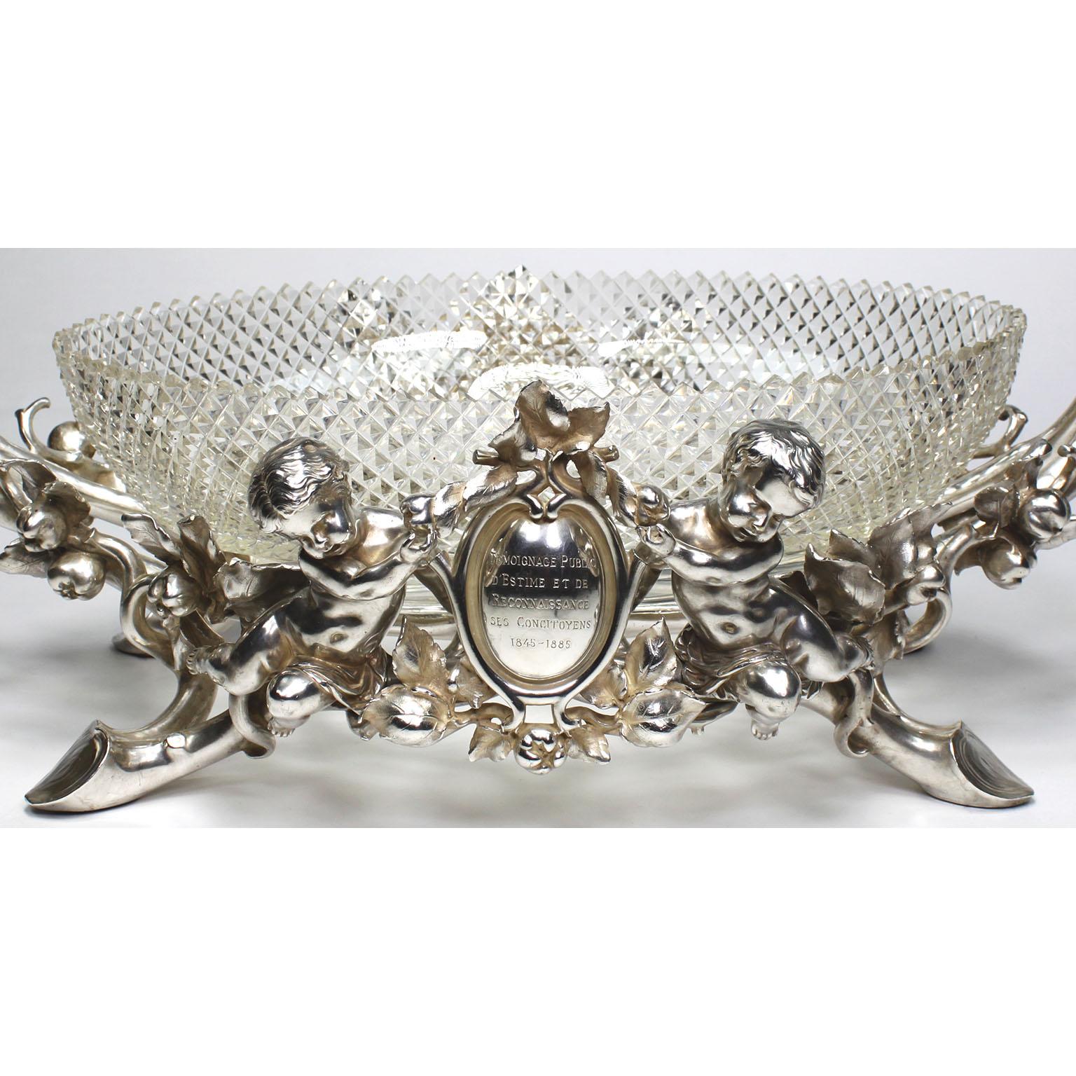 A very fine and palatial French 19th/20th century Christofle & Cie Louis XV style silvered figural centerpiece, fitted with an oval diamond-cut-glass center-dish, attributed to Baccarat, and flanked by two Putti (Children), all on a pomegranate