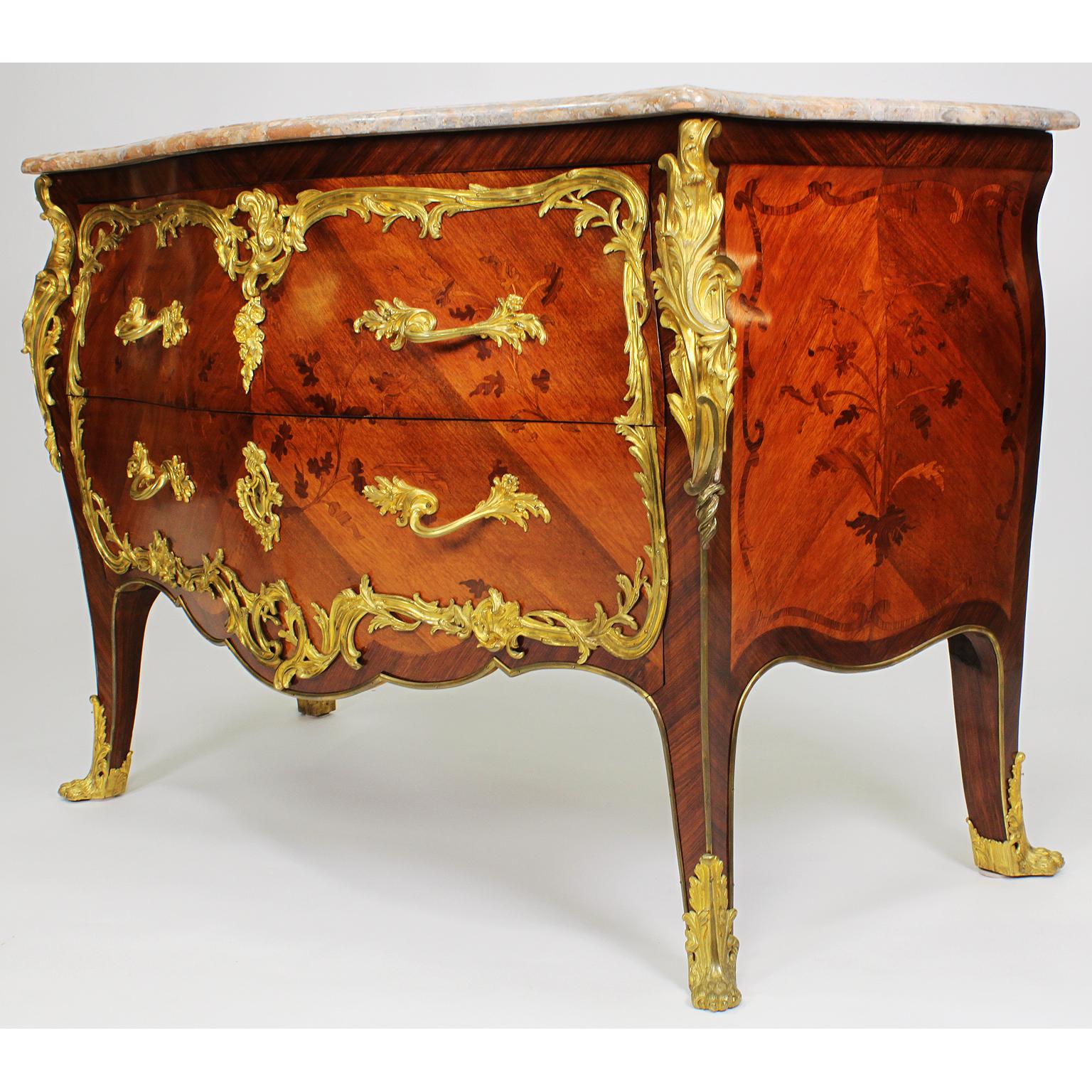A fine French 19th-20th century Louis XV style gilt bronze mounted satinwood and tulipwood Bois Satiné and Bois de Bout floral Marquetry two-drawer commode of bombé serpentine form, with a veined Rivera brown/pink marble top above two long drawers