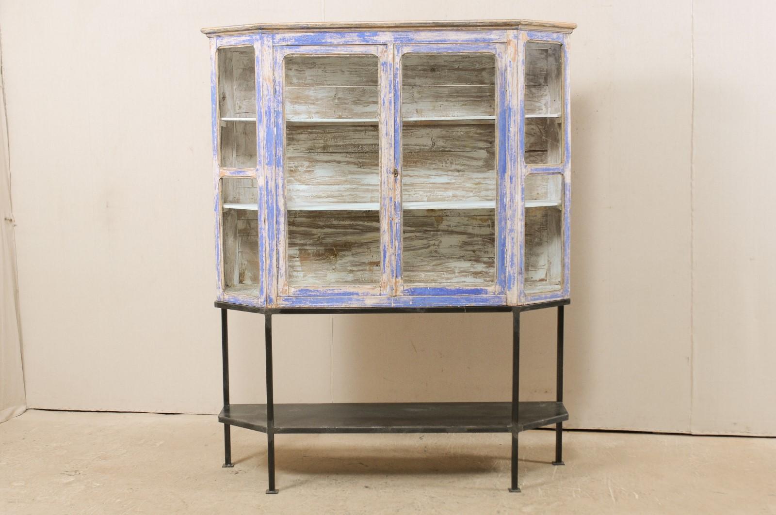 A French glass and wood display cabinet from the 19th century, on newer custom iron base. This antique cabinet from France has a glass display top with two doors at center, and inwardly angled (or canted) glass side windows. It is raised atop a