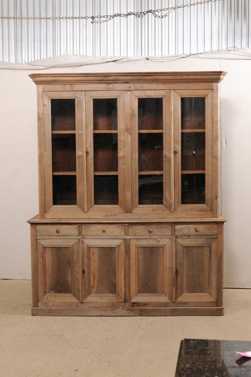 A French tall display and storage cabinet from the 19th century. This antique bleached-wood cabinet from France features a nicely molded cornice, crowning the upper cabinet which houses four glass front doors, and rests atop a lower case fitted with