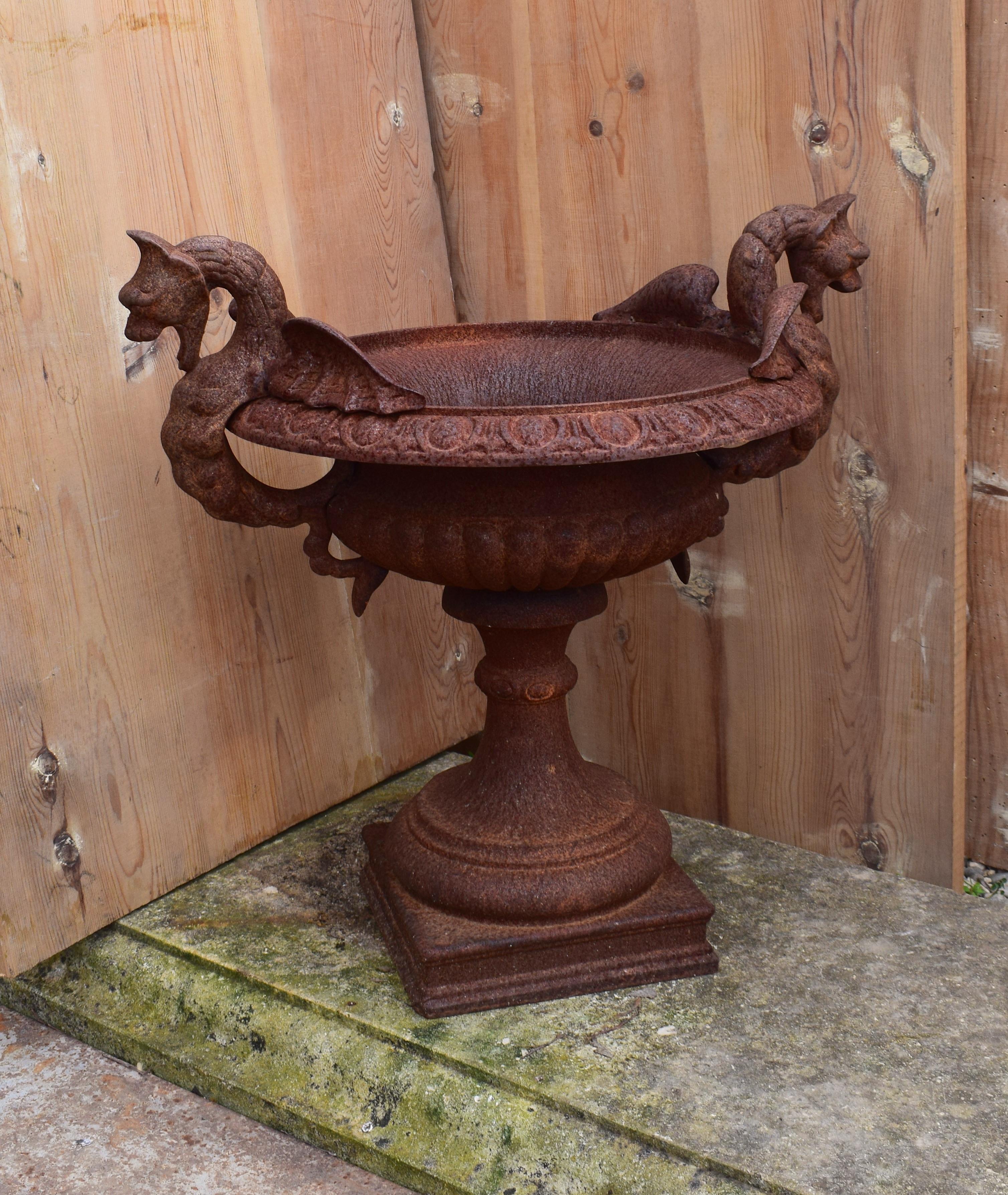 A 19th century heavy cast iron tazza shaped French garden urn. It has a fluted body that is placed upon a square pedestal base. The rim is decorated in an egg and dart pattern and with handles in a dragon design on either side of the urn. This