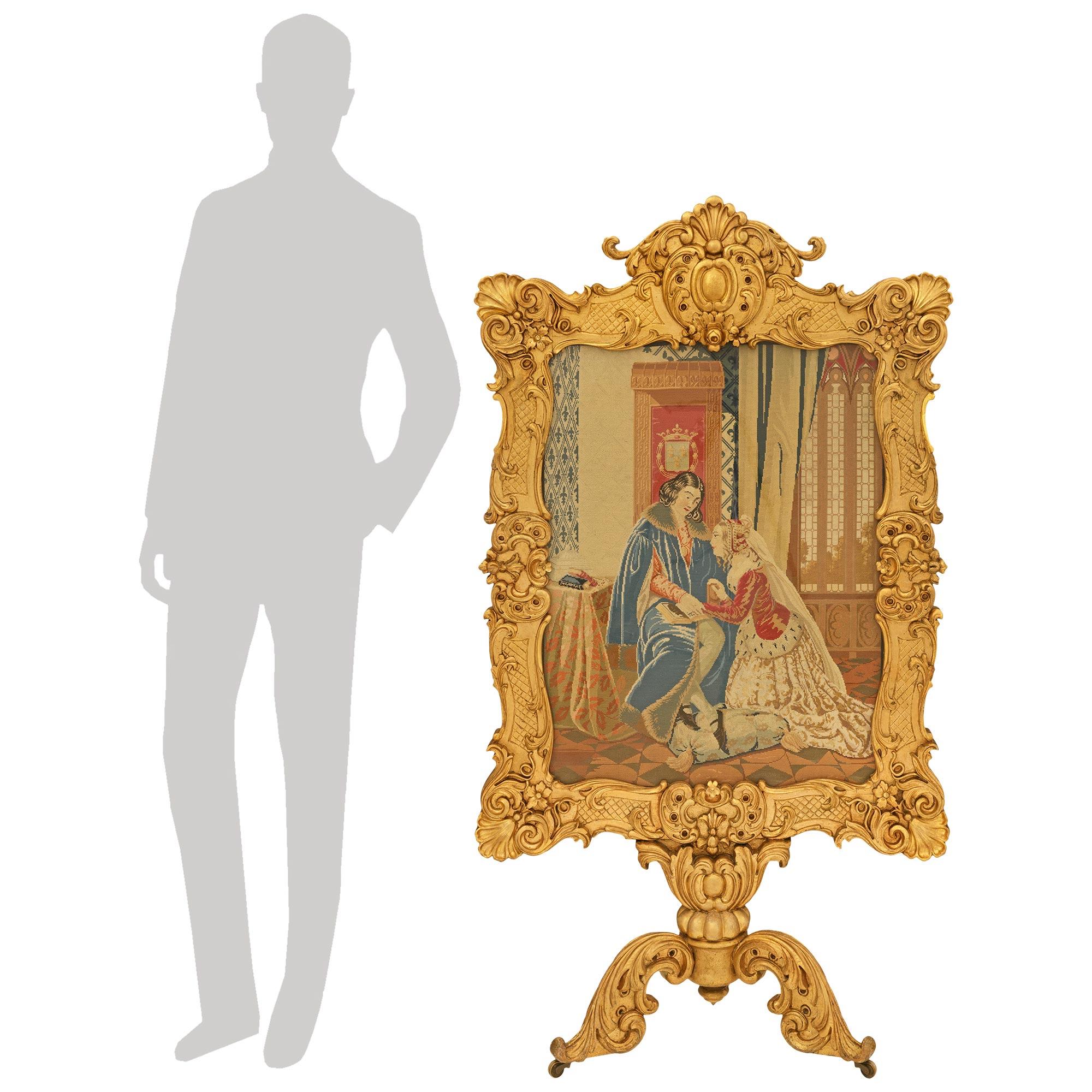 Un paravento indipendente in legno dorato e agugliato del XIX secolo, unico nel suo genere. Questo meraviglioso parafuoco è sollevato da un trio di gambe a volute in legno d'orato su rotelle che conducono a un gambo centrale con decorazioni e alla