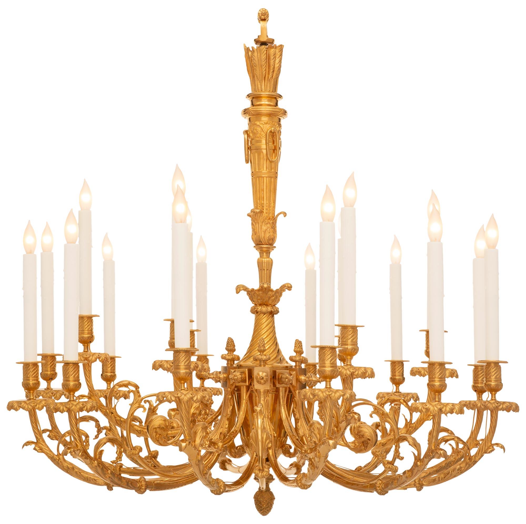 An elegant and large scaled French 19th century Louis XVI st. Ormolu chandelier. The eighteen light chandelier is centered by a richly chased bottom acorn finial leading up to the electrified arms split in two flanking 'C' scrolled arms ending with