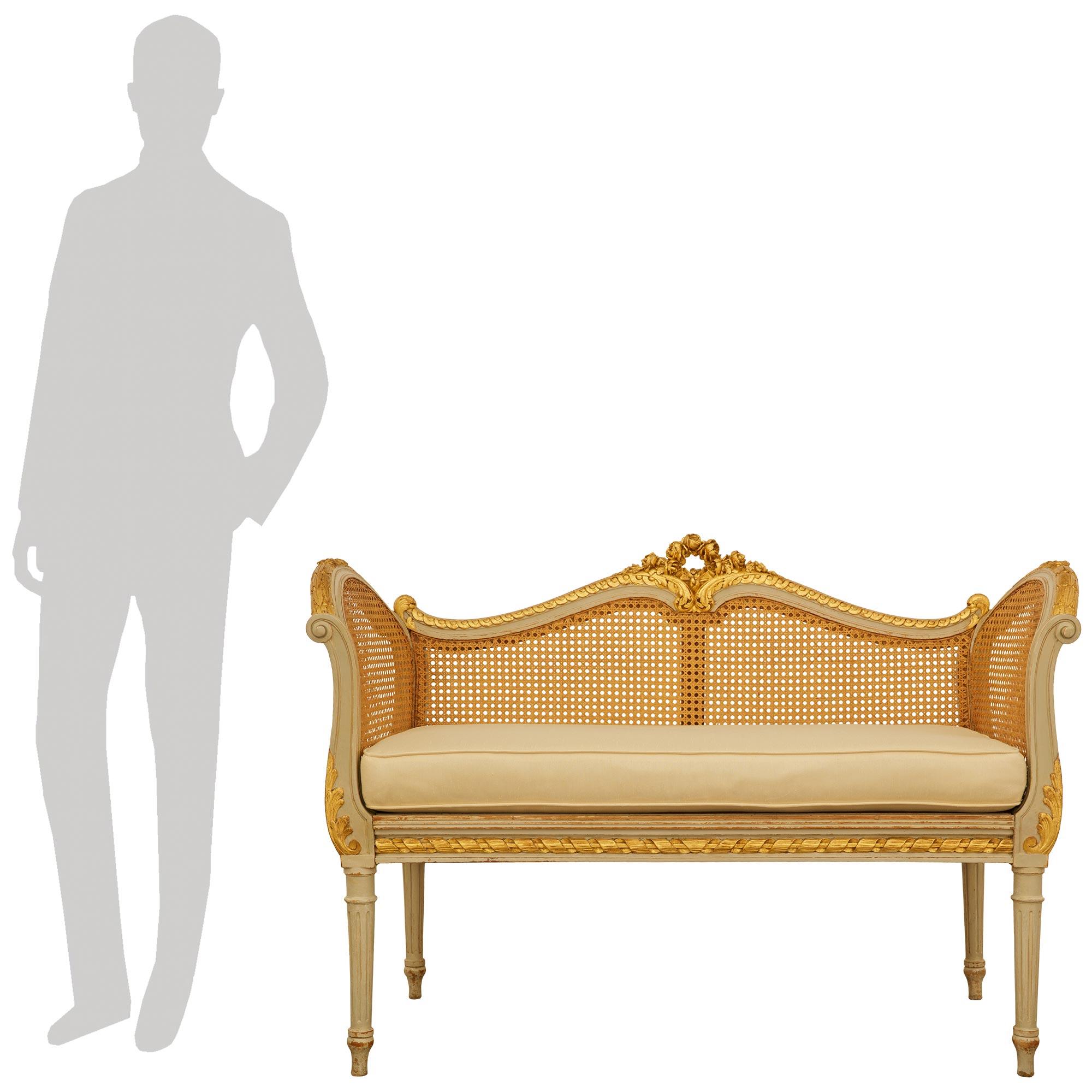 Charmante et très élégante banquette/canapé en bois patiné et doré de style Louis XVI du XIXe siècle. Ce magnifique canapé de petite taille repose sur quatre pieds circulaires fuselés et cannelés, terminés par des pieds en forme de toupie. Le