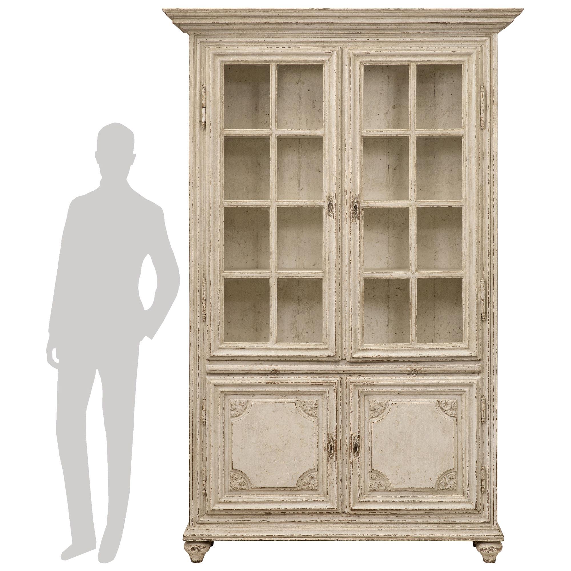 A beautiful and most decorative French 19th century Louis XVI st. patinated wood vitrine cabinet. The four door vitrine is raised by elegant topie shaped feet below the straight mottled border. The two bottom doors display a most decorative recessed