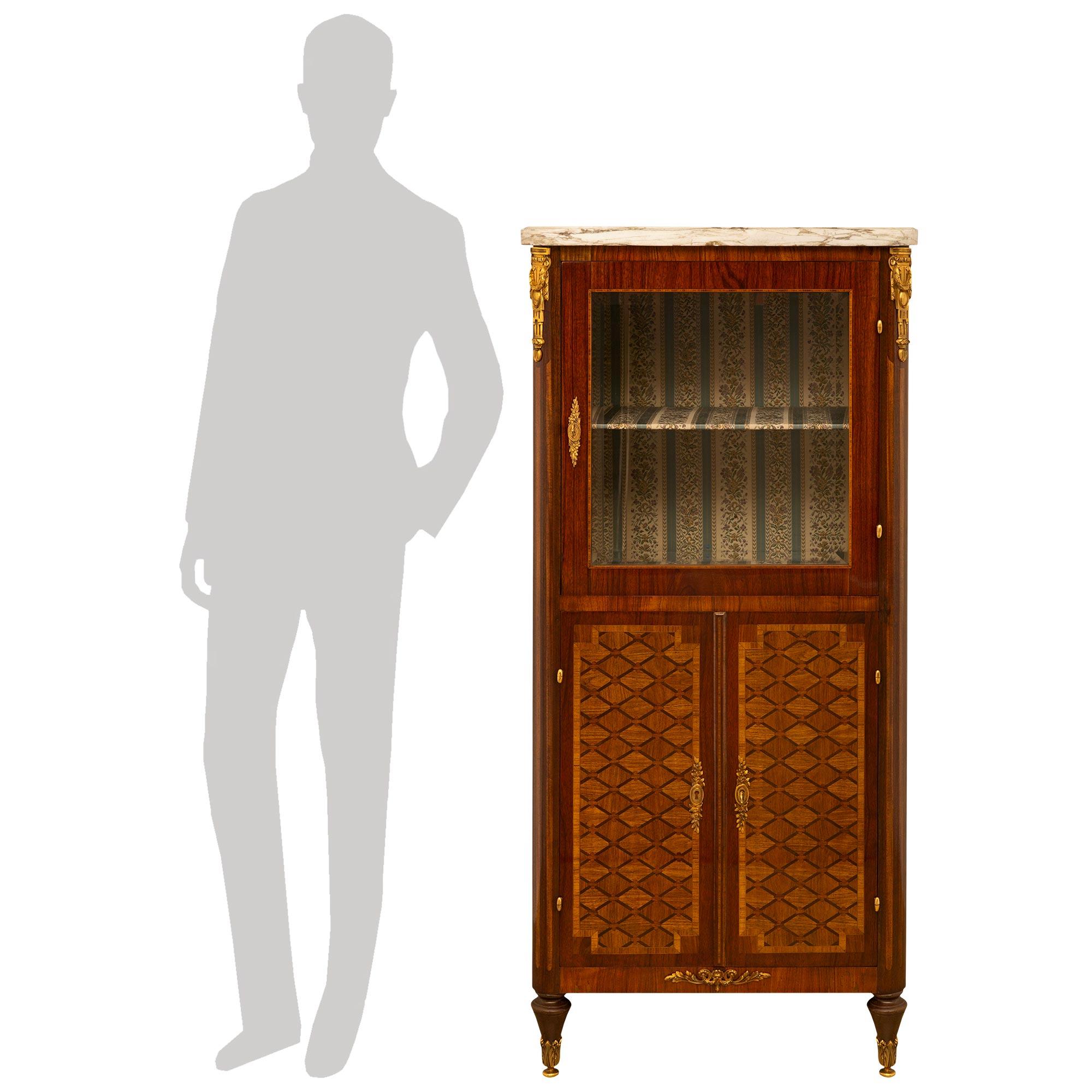 A French 19th Century Louis XVI st. Tulipwood, Kingwood and marble cabinet/vitrine. The vitrine is raised by topie shaped front legs and square tapered legs in the back, with all legs ending with decorative ormolu sabots. The legs flank the straight
