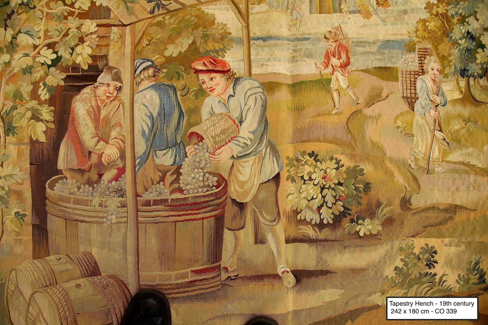 A French tapestry depicting in a bucolic atmosphere the first stage in wine making (gathering the grapes before extracting the juice). The workers, or peasants, bring basketful of white grapes and tumble their contents into a big vat, constructed of