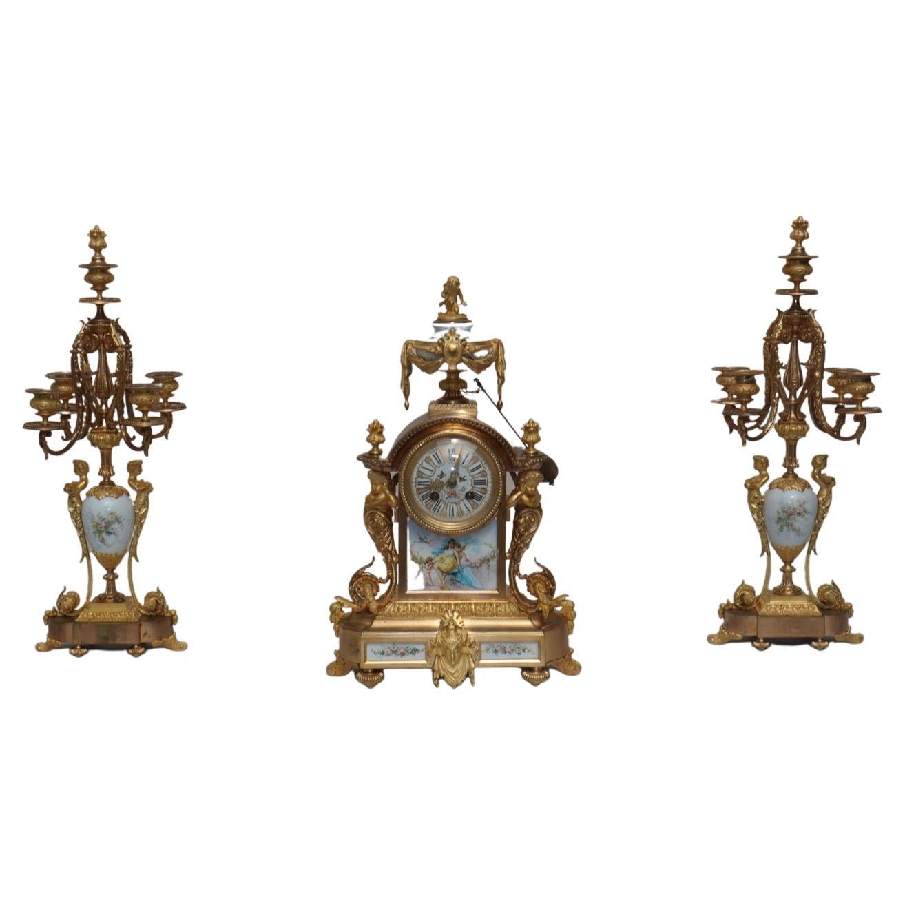“Love”
A French Ormolu-Mounted, White-ground Sèvres Style Porcelain Three-Piece Clock Garniture
The clock with a hand-painted polychrome porcelain plaque decorated with a woman on clouds surrounded by Putti and lovebirds symbolizing Love, the