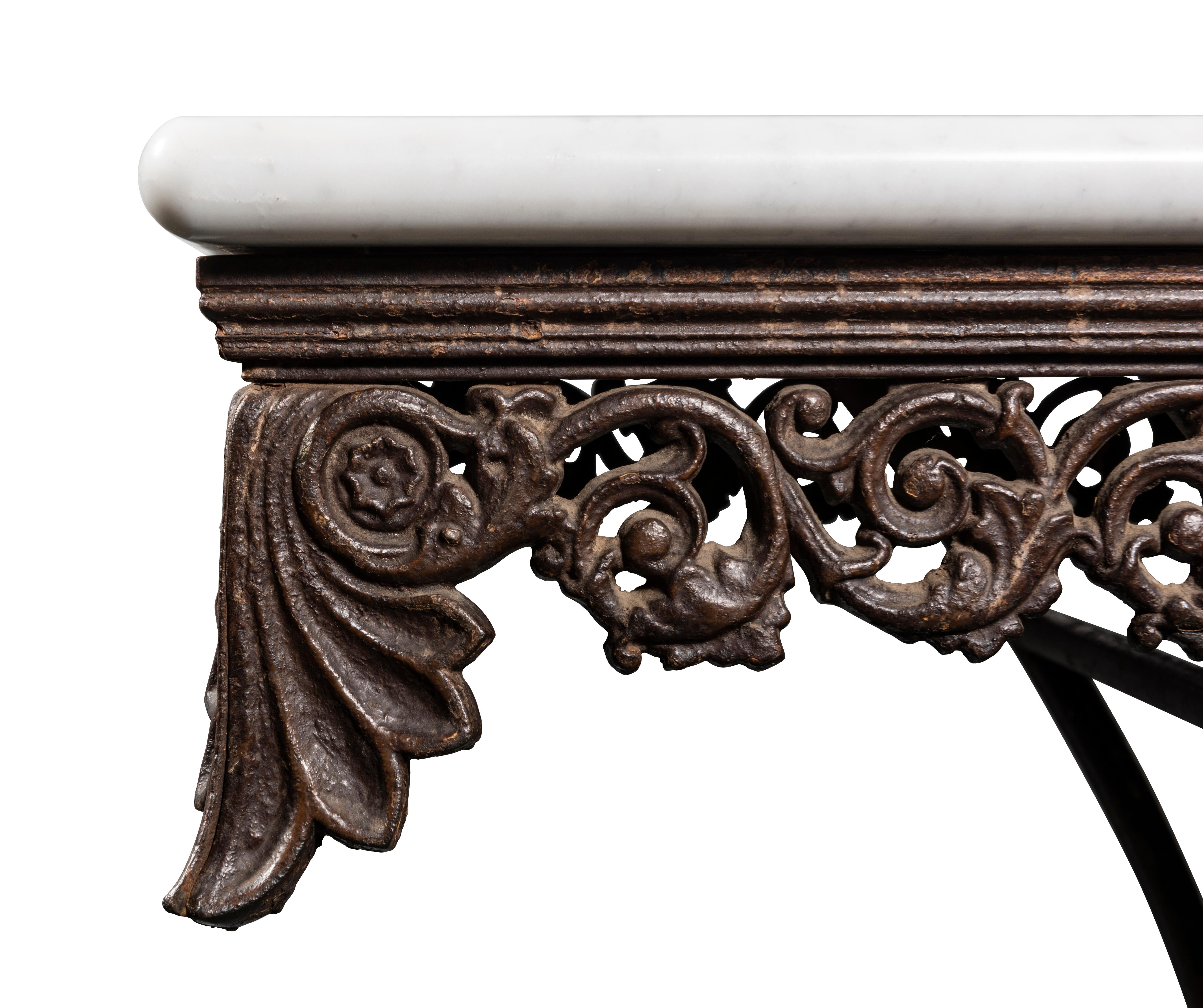 The white marble top with rounded edge over iron frieze of ornately cast foliated scrolls centred with palmette, a further palmette on each corner and conforming decoration continuing to the sides, supported on four scroll legs joined by central