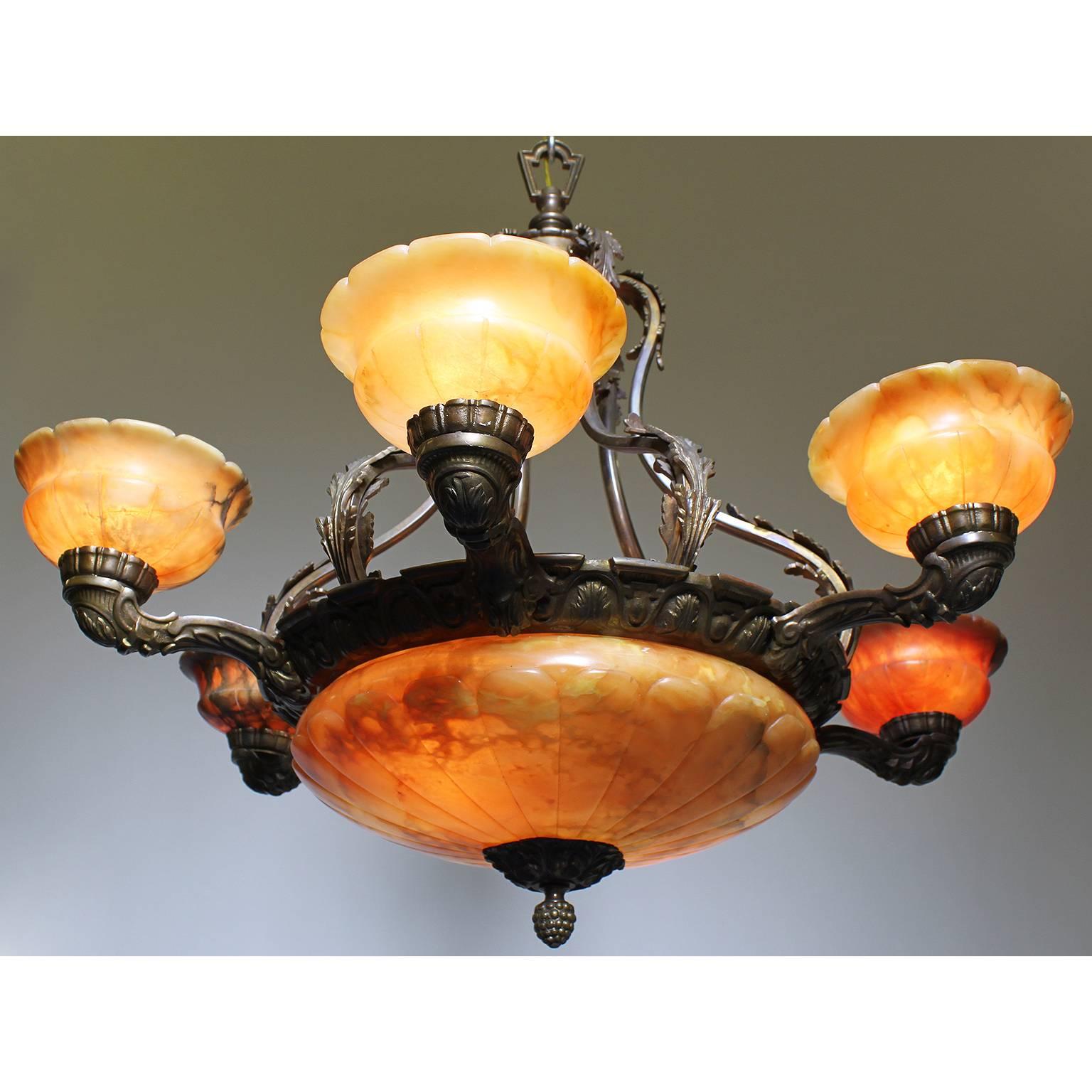 A French 20th century Art Deco and bronze carved veined caramel-colored alabaster six-light chandelier. The carved circular alabaster plafonnier with a floral apron and banded frame with six alabaster lights supported by cornucopia shaped bronze