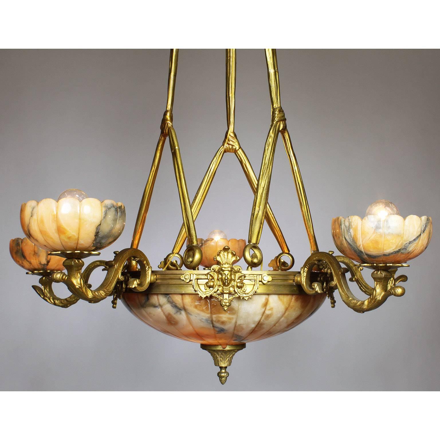 A French 20th century Art-Deco style gilt bronze and caramel-colored carved alabaster five-light chandelier. The circular banded bronze frame surmounted female masks and five 