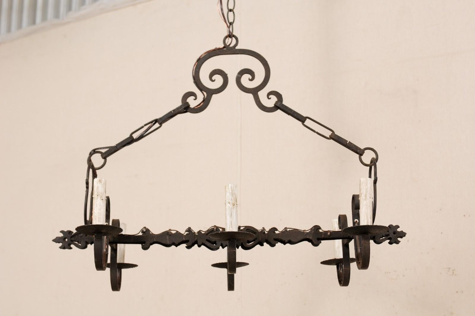 A French six-light iron chandelier from the mid-20th century. This vintage chandelier from France has an over-all rectangular-shaped appearance with a pair of horizontally set, decoratively cut and pierced iron bars making up the center, giving