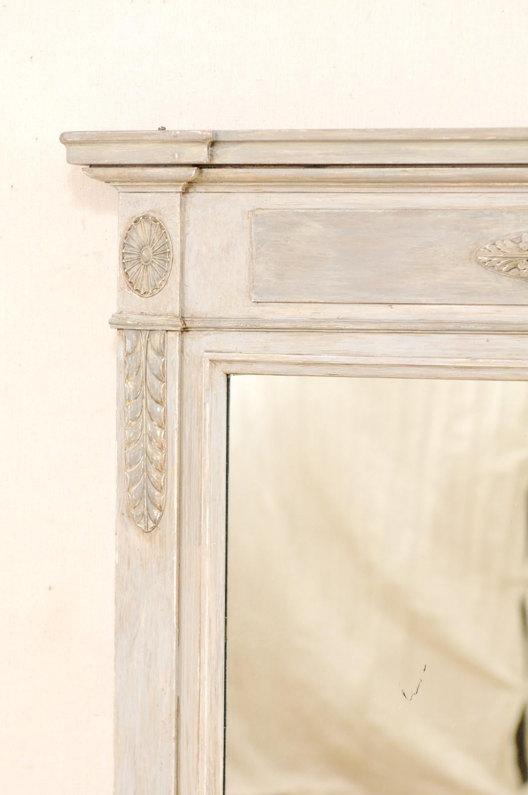 A French painted wood mirror from the mid-20th century This vintage mirror from France features a rectangular-shaped frame with clean lines accented with column style sides and adorn with carved medallions of foliage and leaf motif about the upper