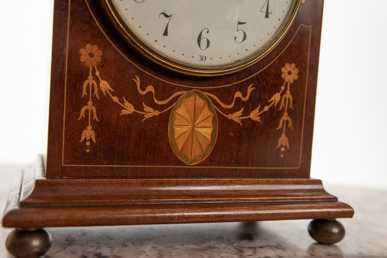 A very attractive 8 day striking the hours and half hours mantel clock. With round bowed white dial with Arabic numerals contained in a stunning mahogany inlaid case of the highest quality, with brass carrying handle to the top and four brass ball