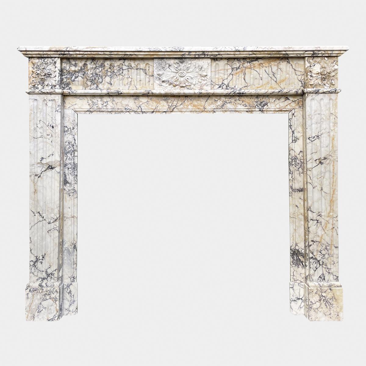 A French antique fireplace in the Louis XVI style carved in Italian Seravezza Marble. The fluted jambs with deep side returns and inner slips, terminating in square carved Patarae corner blocks. The frieze of conforming design with fluted panels