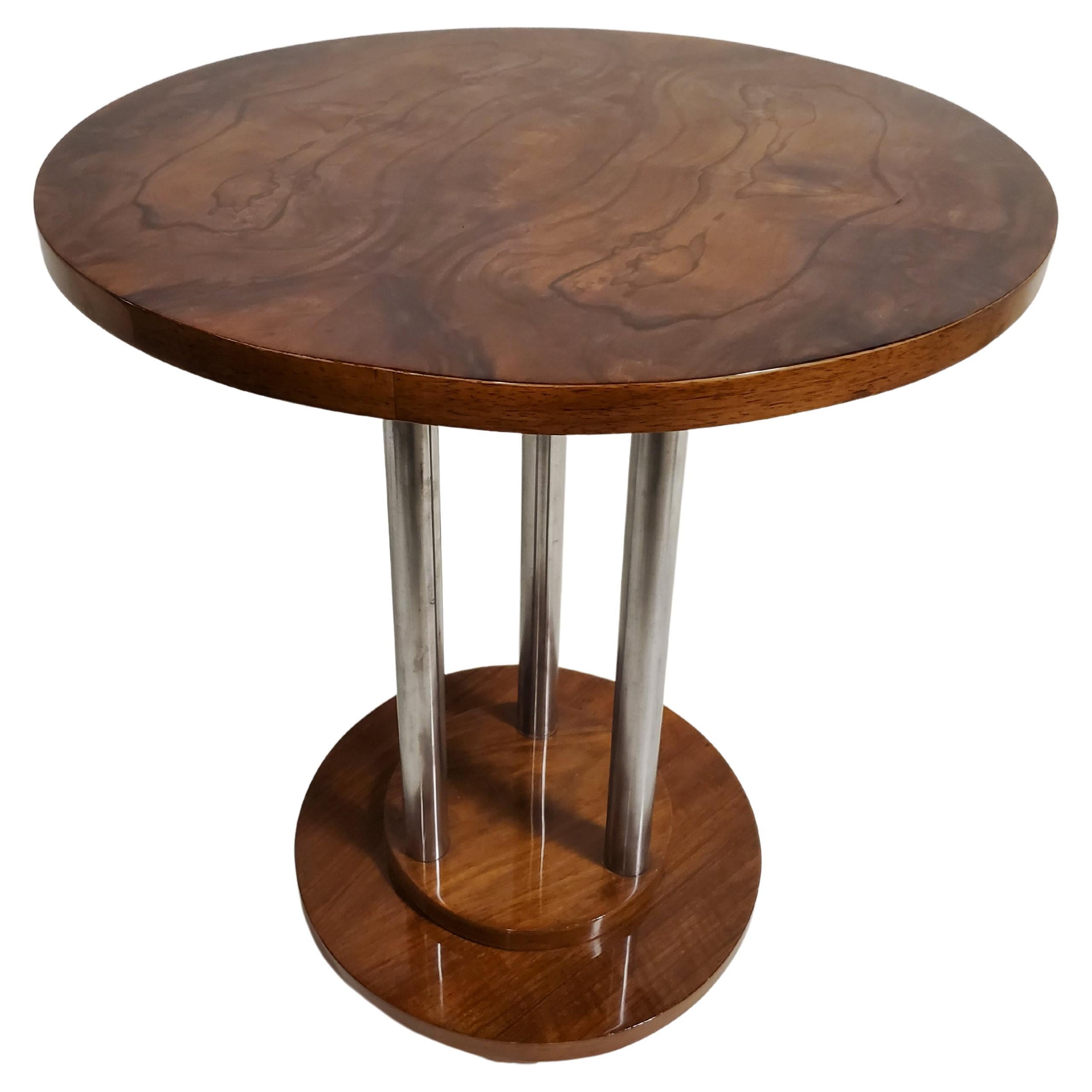 A French Art Deco walnut side table highlighted by nickeled metal accents. Three tubular metal poles support a beautifully grained, book matched circular wood top with an organic fully grained pattern, that rest on a circular stepped base ending