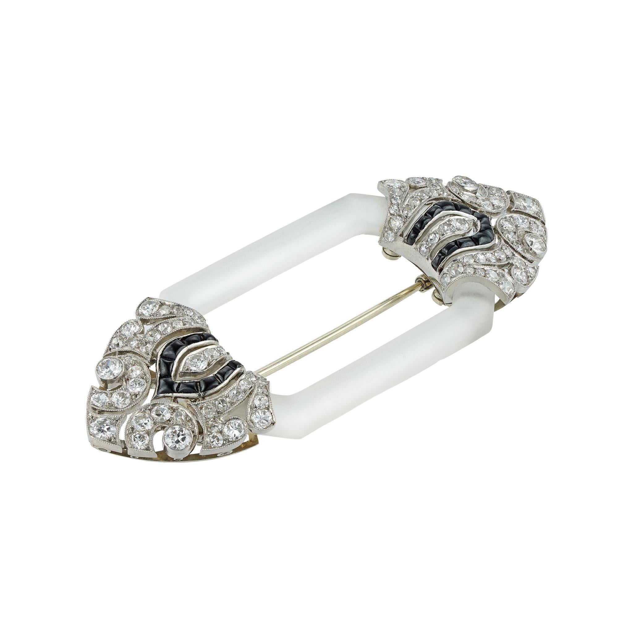A French Art Deco crystal, diamond and onyx brooch by Chaumet, consisting of an octagonal-shaped frosted rock crystal frame, mounted between two finials of palmette design, with diamond-set scroll Mughal style decorations, accented by a line of