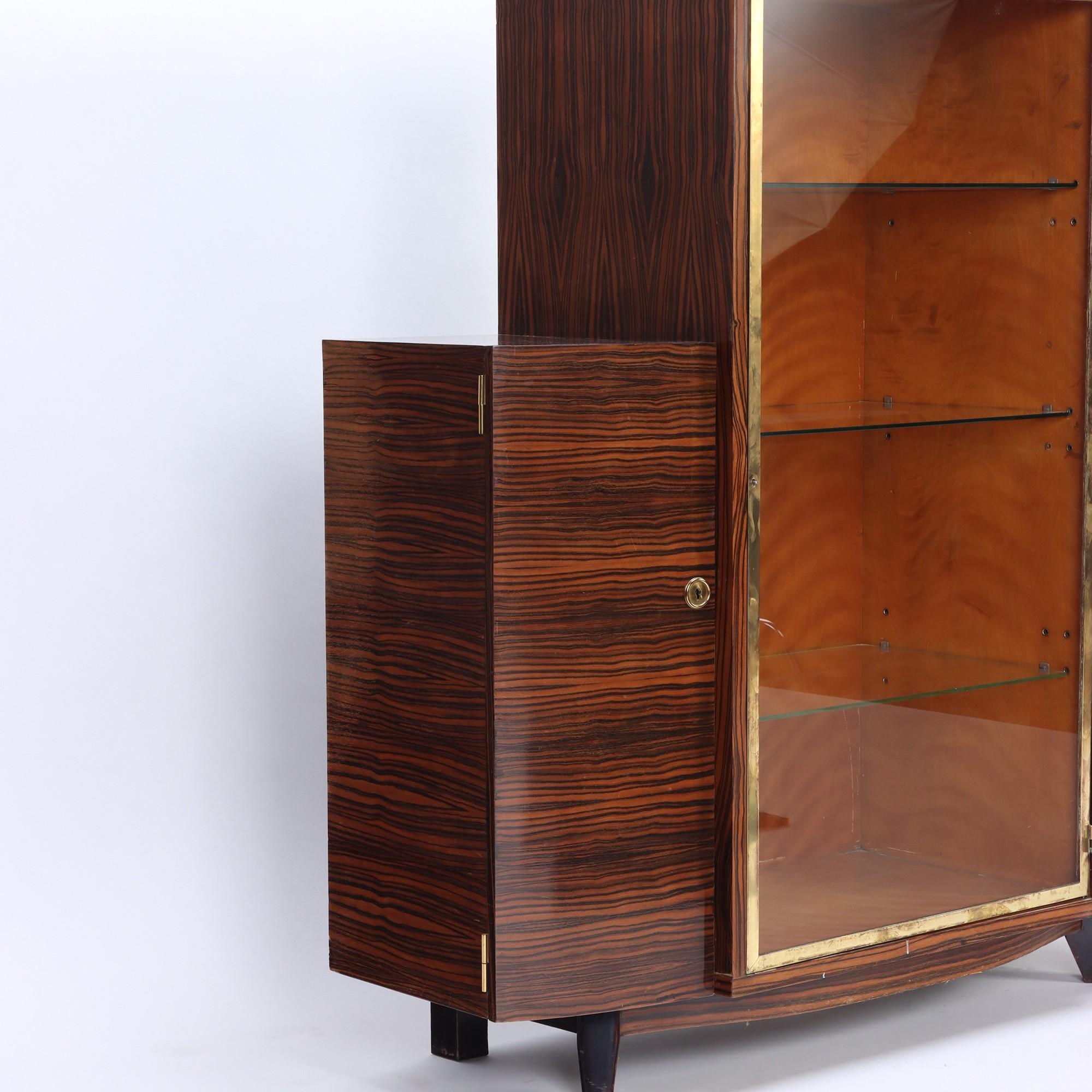 An elegant French Art Deco macassar cabinet, having a bronze and glass door opening to glass shelves for display. Cabinet is flanked by drawers on either side. C 1935.